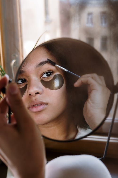Mujer sosteniendo un espejo mientras maquilla sus pestañas. | Foto: Pexels