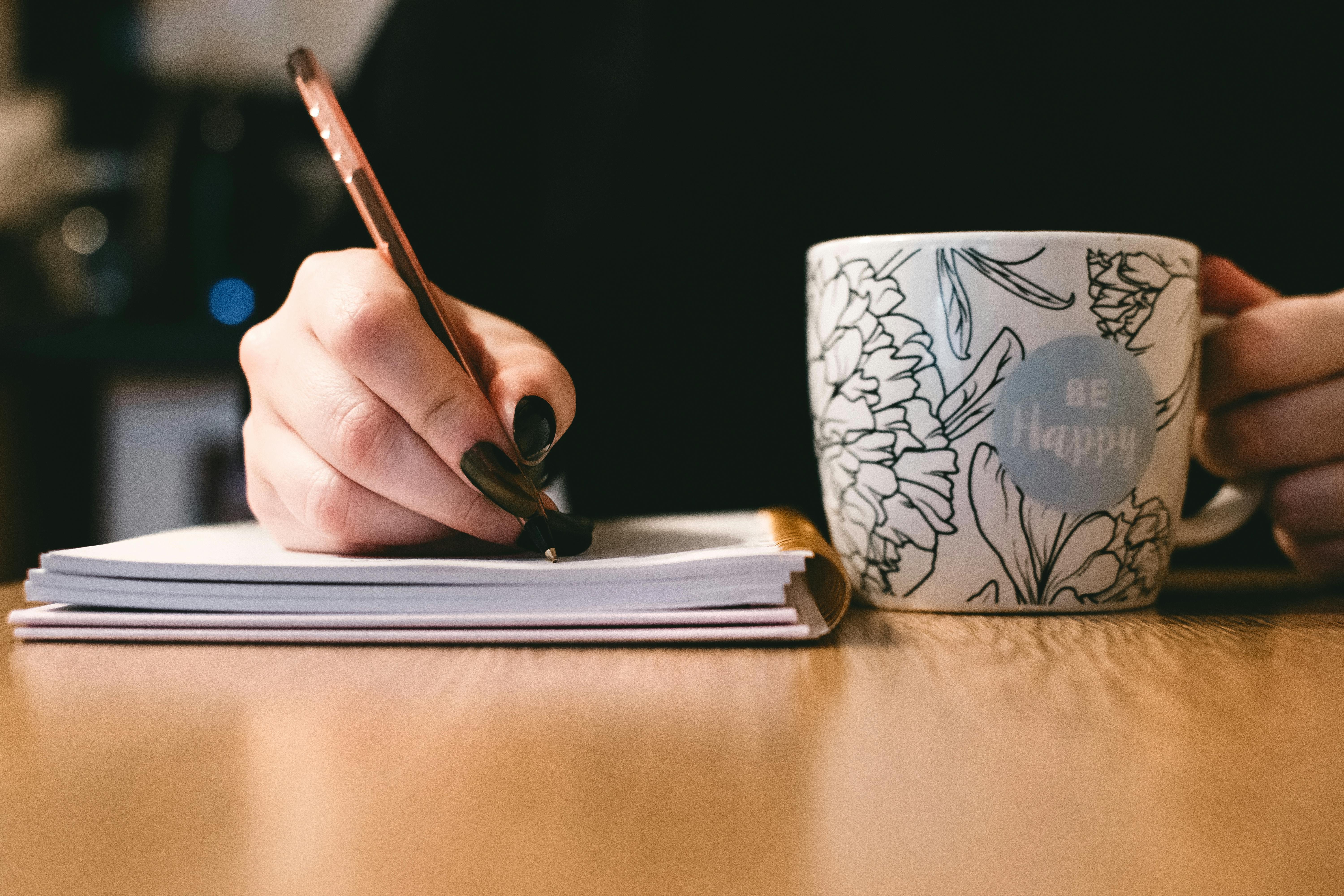 Una mujer escribiendo en un bloc de notas con una taza de café cerca | Fuente: Pexels