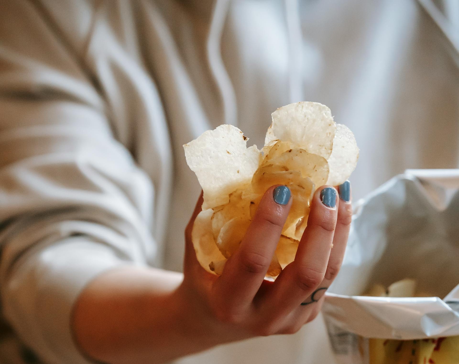 Una mujer con un puñado de patatas fritas | Fuente: Pexels