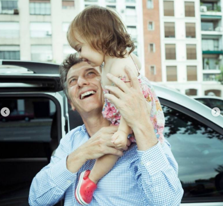 Con una sonrisa radiante, Mauricio Macri carga a la pequeña Antonia sobre sus hombros junto a un vehículo. La niña, vestida con un solero floreado y calzado rojo, sonríe divertida mientras su padre la sostiene con firmeza en un día soleado de paseo familiar. | Fuente: Instagram/mauriciomacri