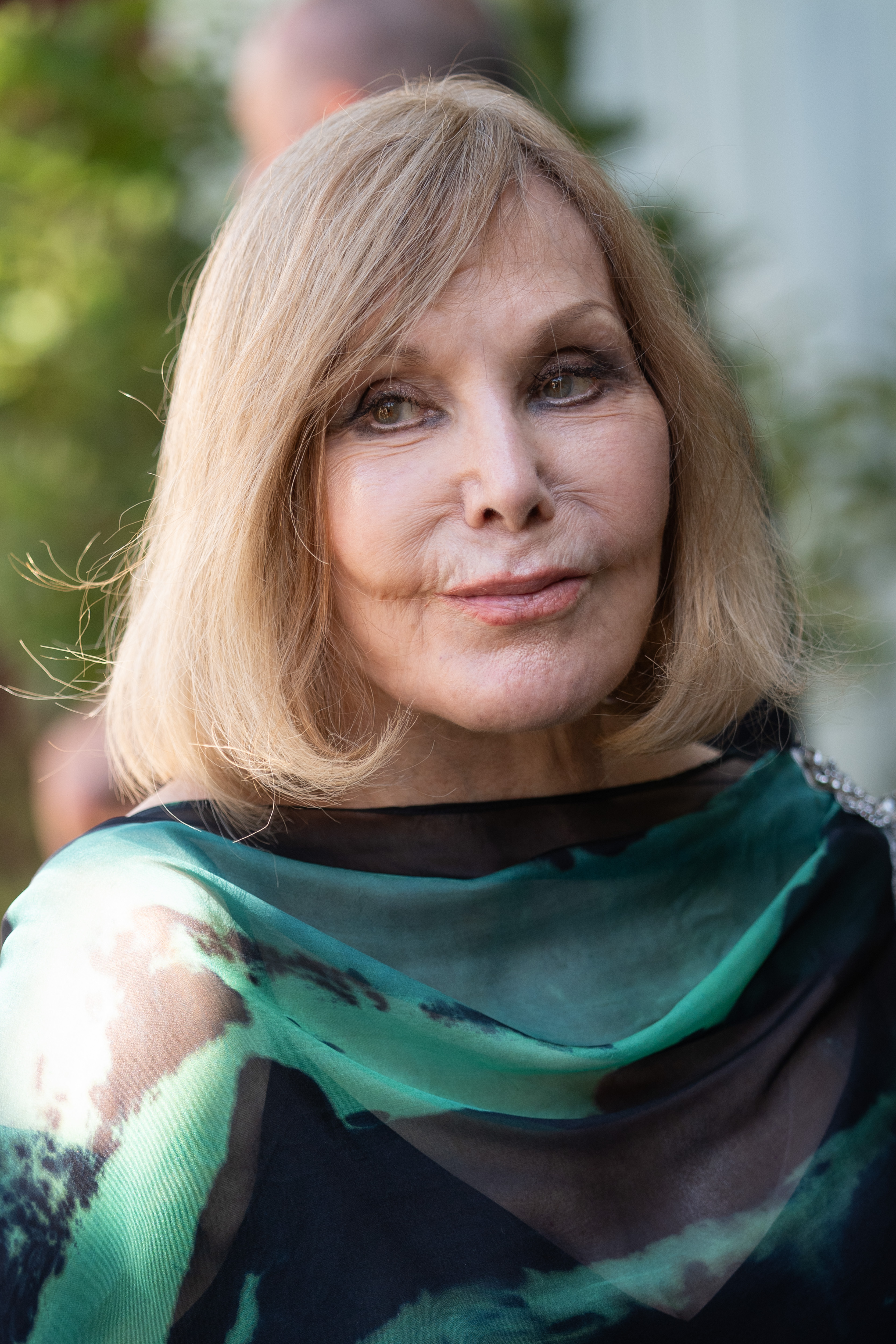 Kim Novak posa para un primer plano en el 82.º Festival Internacional de Cine de Venecia, con un chal en tonos verde azulado y verde sobre un conjunto negro. Su corte de pelo rubio a lo bob le enmarca la cara mientras mira ligeramente hacia un lado. | Fuente: Getty Images