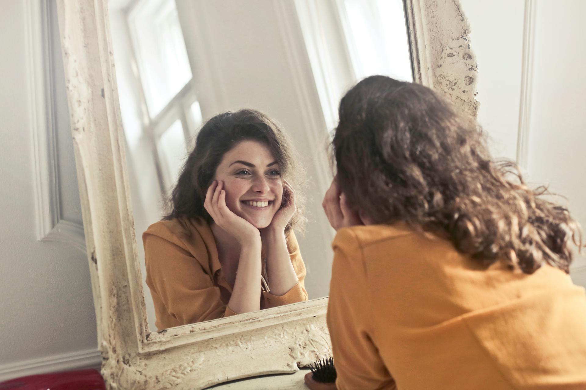 Una mujer sonriente mirando su reflejo en el espejo | Fuente: Pexels
