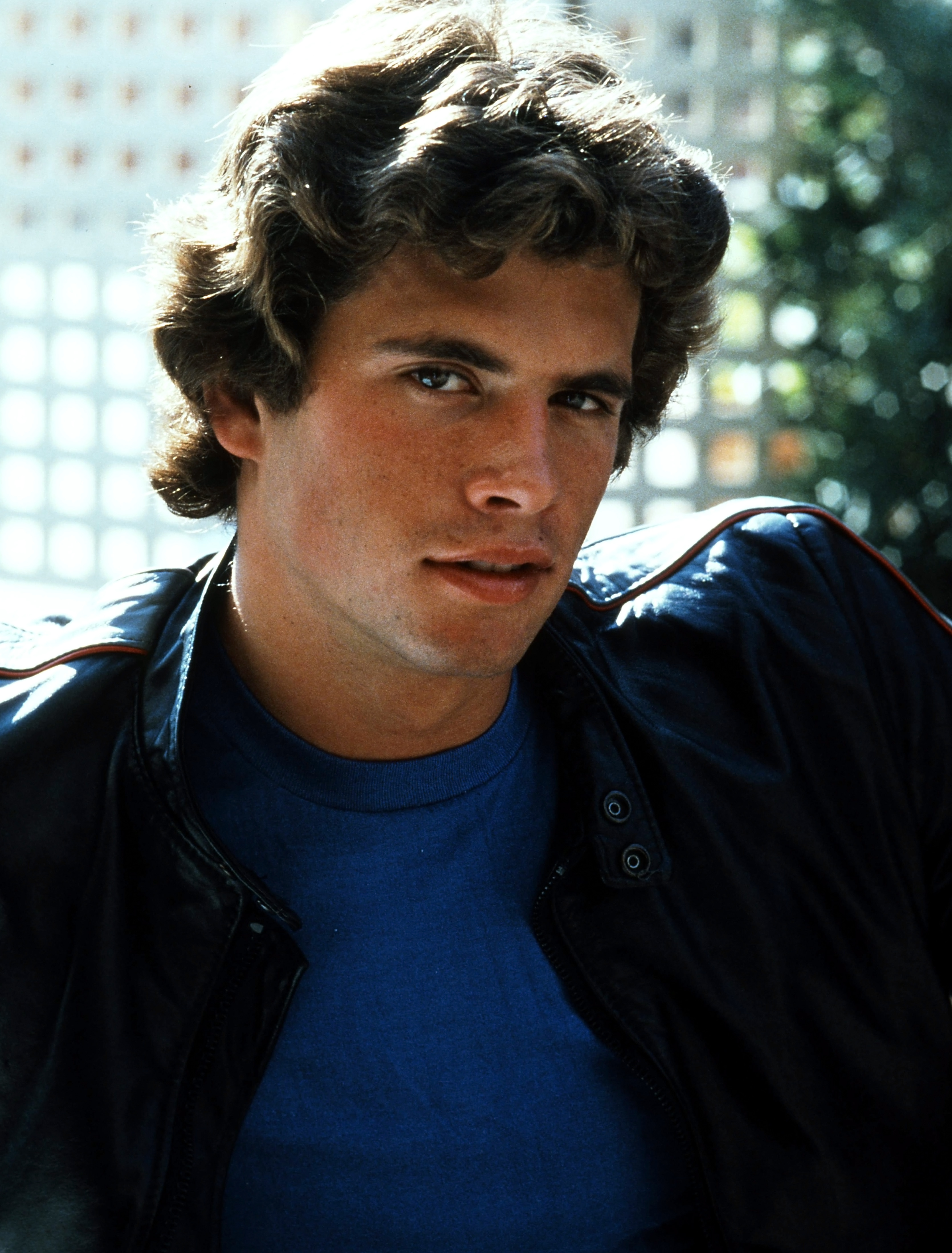 Este actor en ascenso desprende una elegancia natural en un retrato en color de estilo vintage de alrededor de 1978. Con una camiseta de cuello redondo de un azul intenso bajo una chaqueta de cuero negra con ribetes rojos, mira a la cámara con una melena castaña rizada y voluminosa, bañada por el sol, y unos rasgos marcados y bien definidos. | Fuente: Getty Images