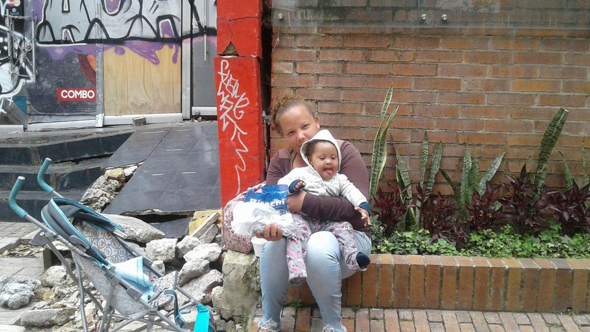 Imagen referencial. Mujer sin hogar sentada con su hija sobre su regazo en una acera. | Foto: PxHere