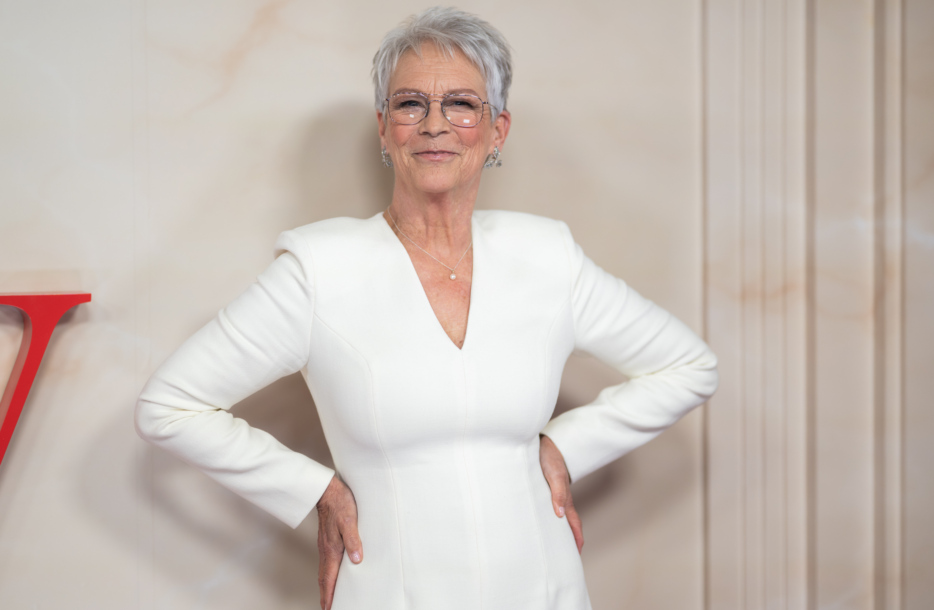 Curtis sonríe con un atuendo blanco y anteojos en una proyección especial de "Ella McCay" en Londres el 24 de noviembre de 2025. Su cabello corto y plateado se ha convertido en uno de sus looks más reconocibles. | Fuente: Getty Images