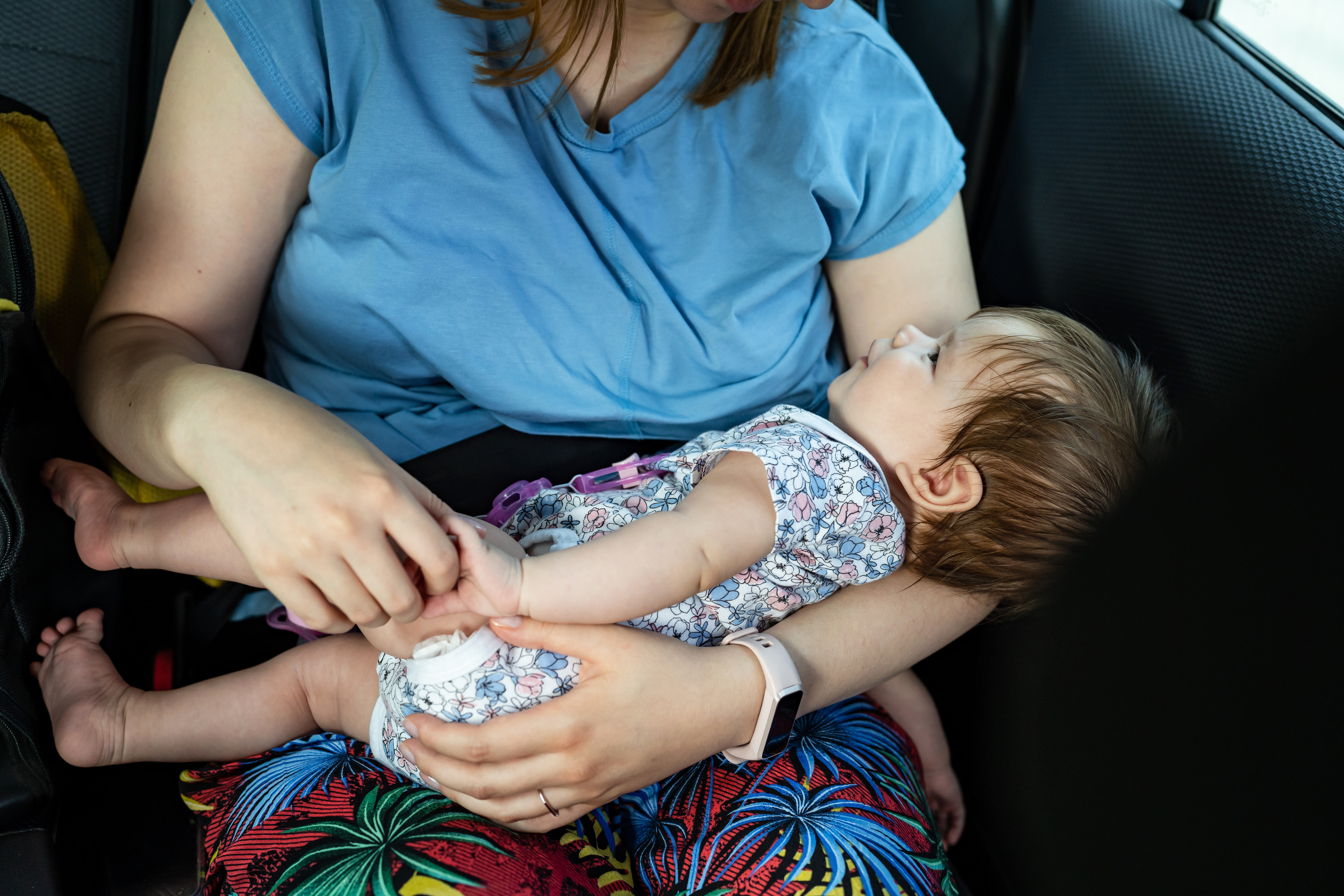 Bebé de cuatro meses en el regazo de su madre desconocida que la sostiene en el asiento trasero del Automóvil. | Fuente: Shutterstock