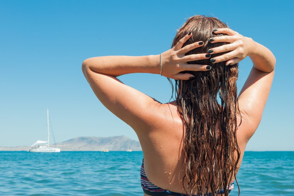 Mujer sosteniendo su cabello húmedo mirando hacia el mar. | Foto: Shutterstock