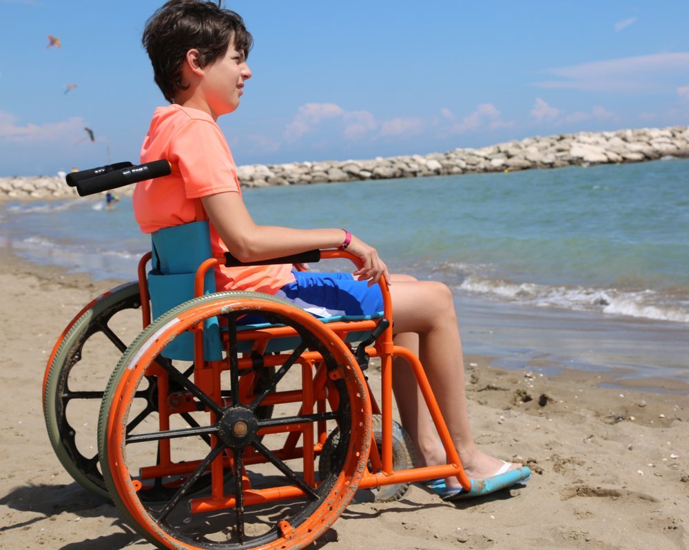 Joven en silla de ruedas con ruedas grandes para moverse sin problemas en la arena de la playa junto al mar en verano. Fuente: Shutterstock