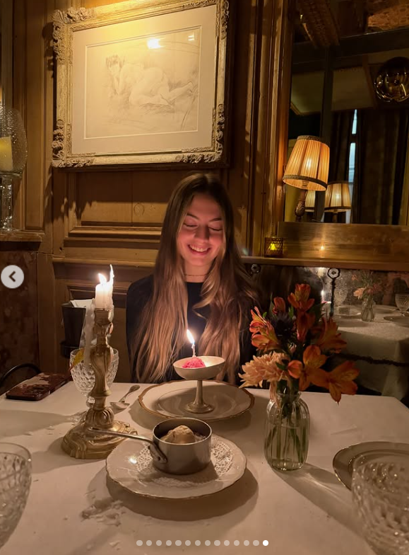 Antonia Macri sonríe frente a una pequeña copa con una vela de cumpleaños encendida en un íntimo restaurante parisino iluminado con candelabros, acompañada de un arreglo de flores otoñales y postres servidos en la mesa. | Fuente: Instagram/juliana.awada