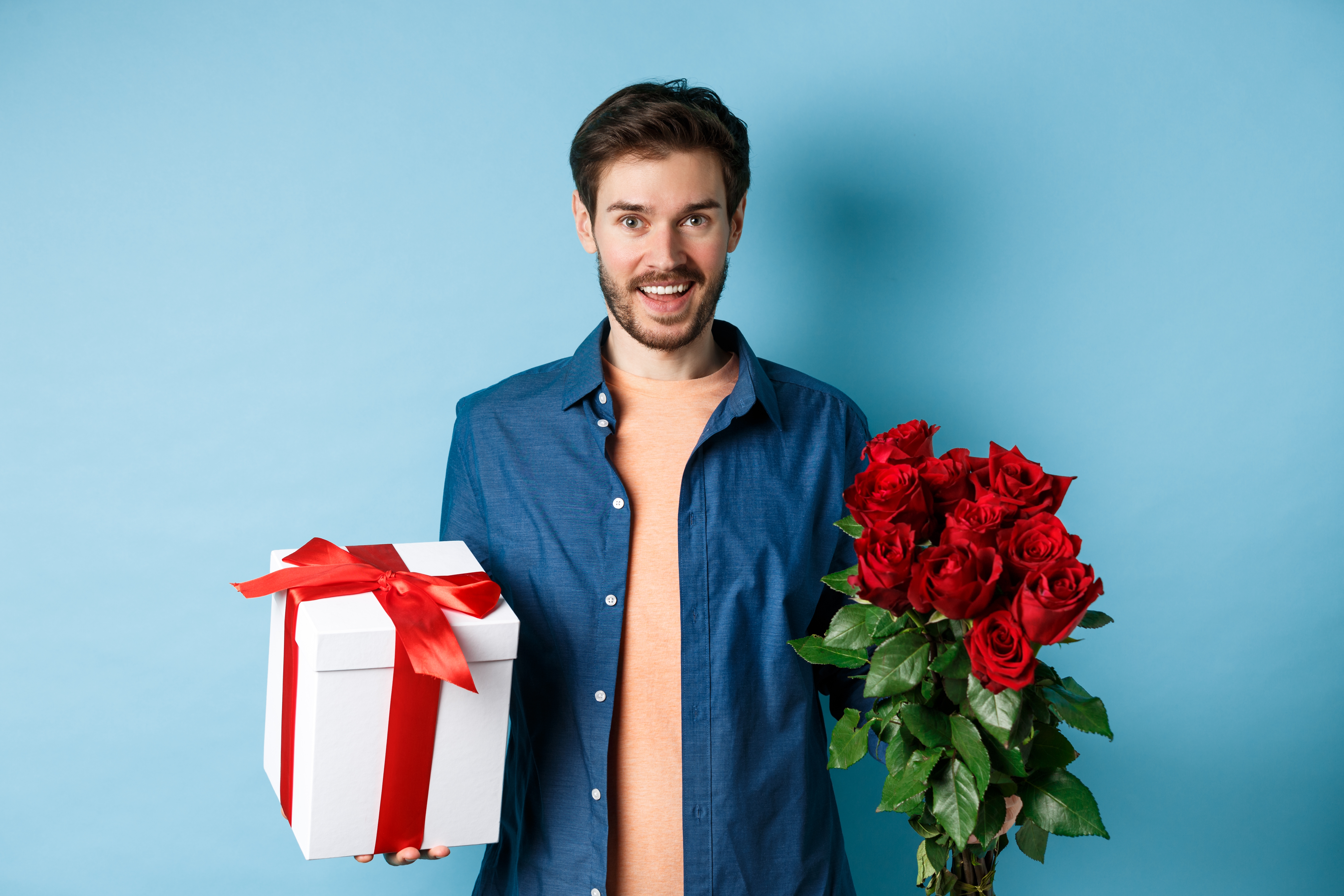 Joven feliz llevando flores y regalo en cita romántica. | Fuente: Shutterstock
