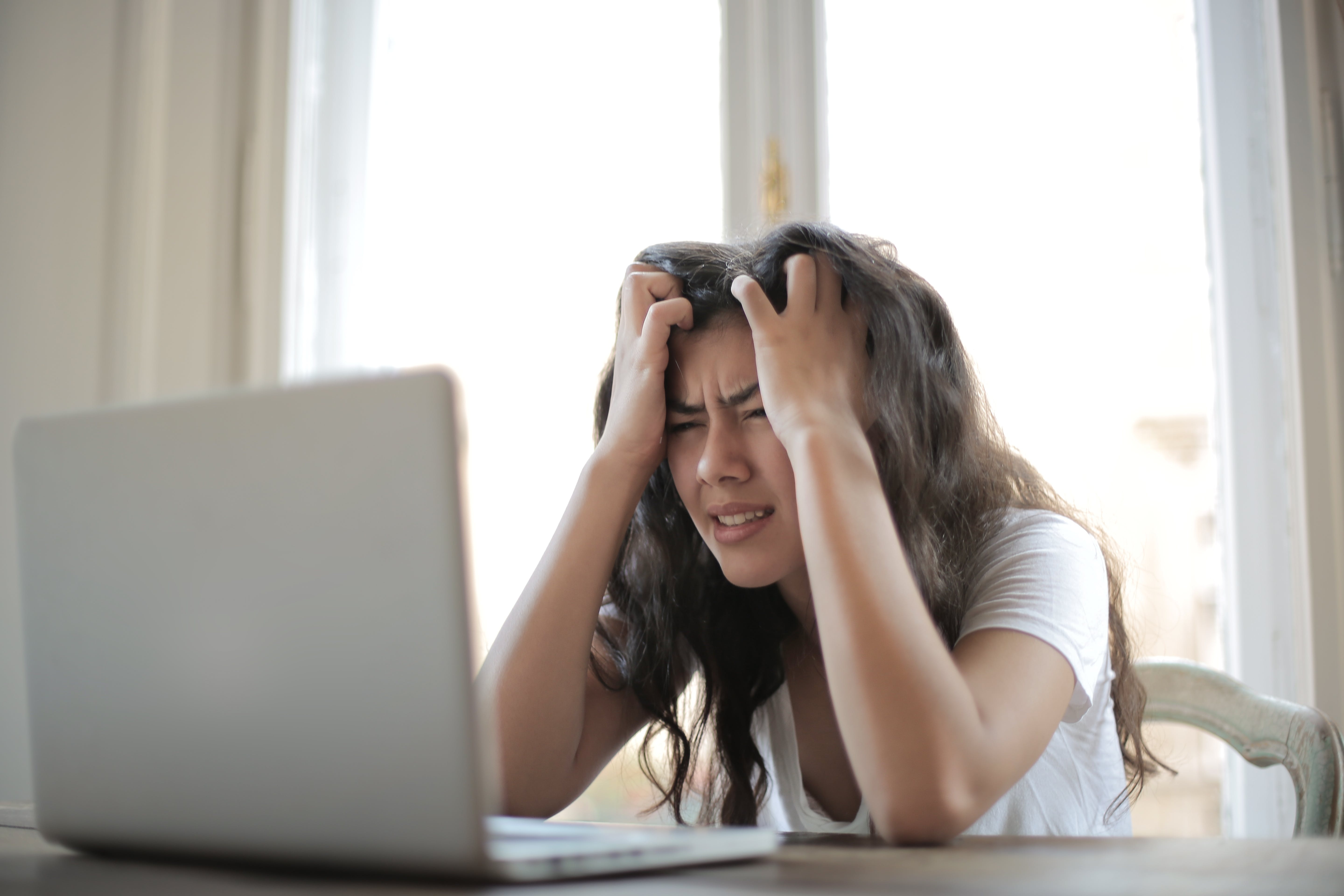 Una mujer frustrada se pasa las manos por el pelo mientras mira un portátil | Foto: Pexels