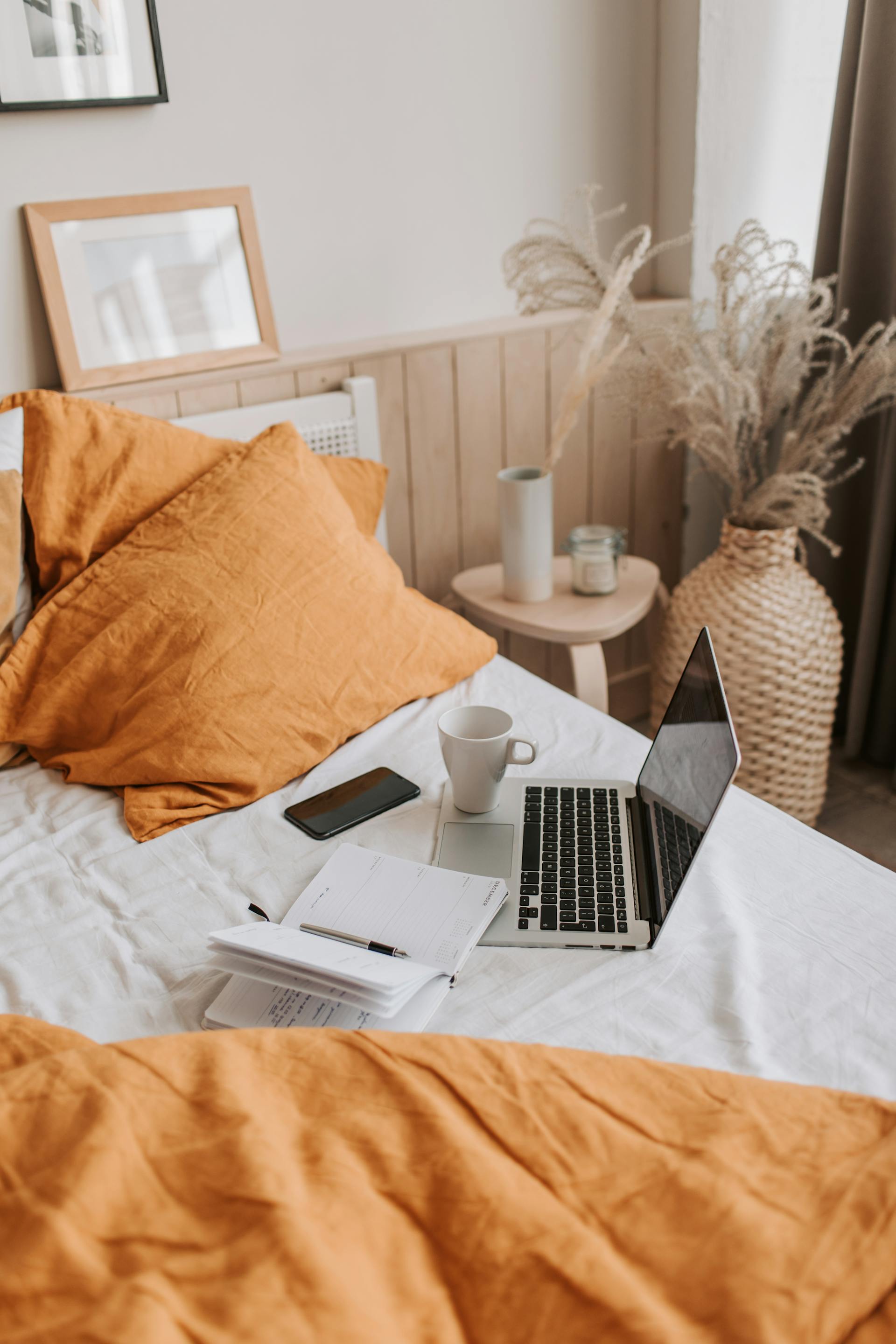 Una taza de café y un portátil sobre una cama | Fuente: Pexels