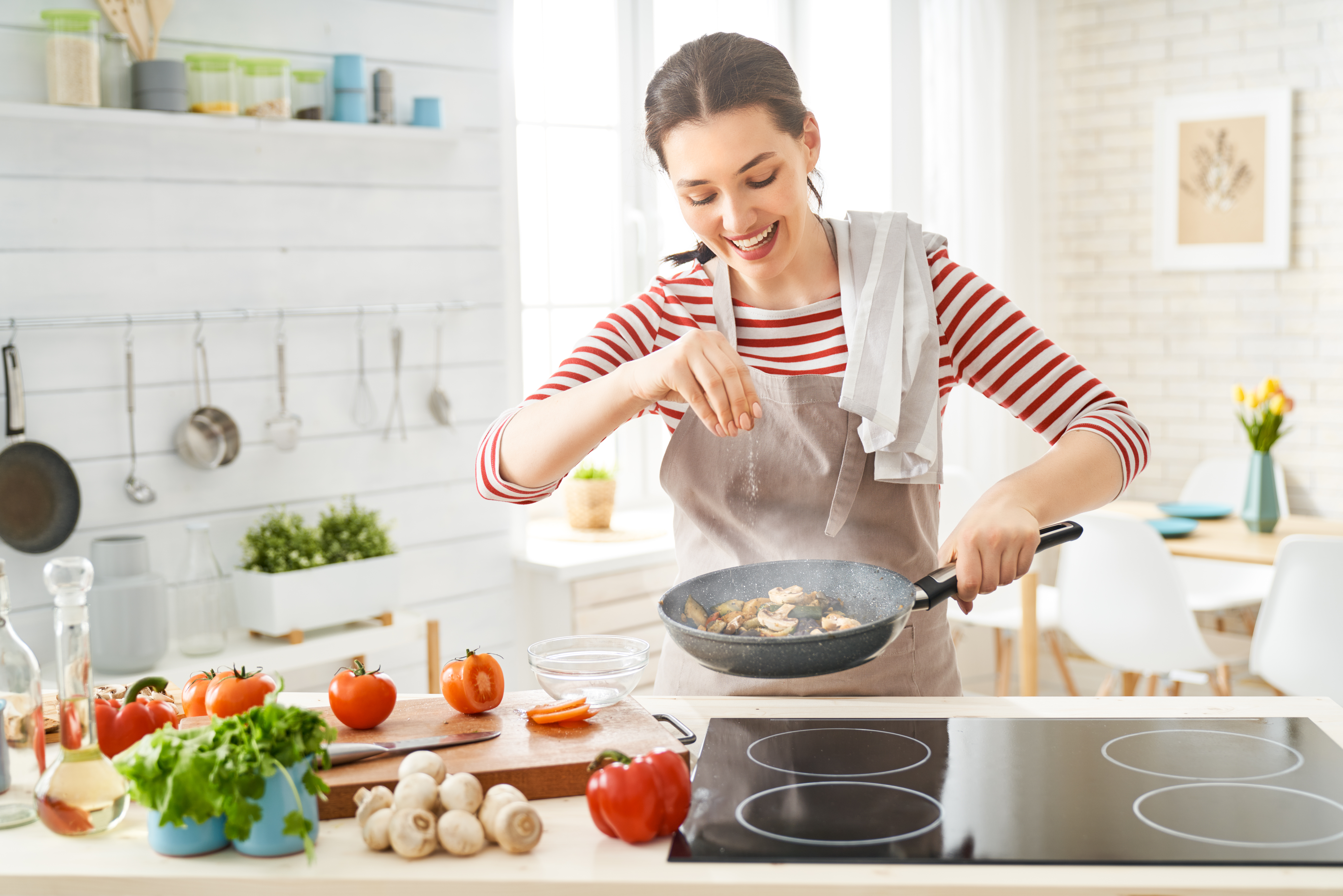 Una mujer feliz está preparando la comida adecuada en la cocina. | Fuente: Shutterstock