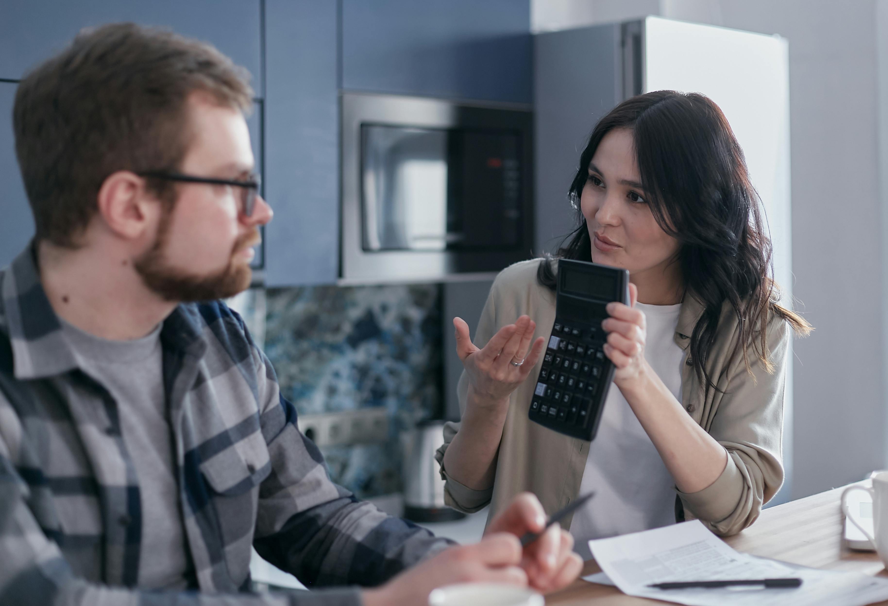 Un hombre y una mujer sentados a la mesa mientras ella le enseña una calculadora | Fuente: Pexels