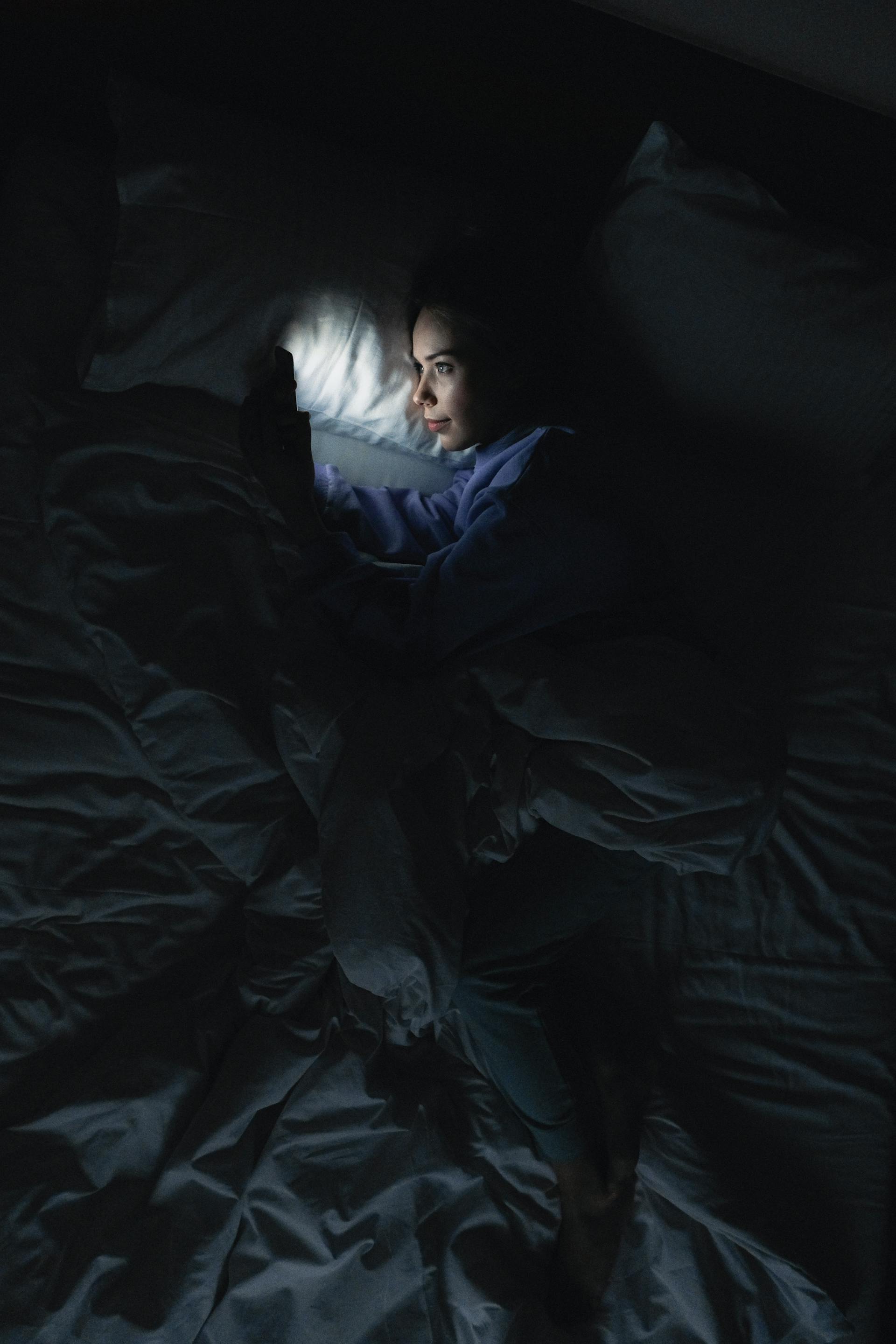 Una mujer usando su teléfono en la cama | Foto: Pexels