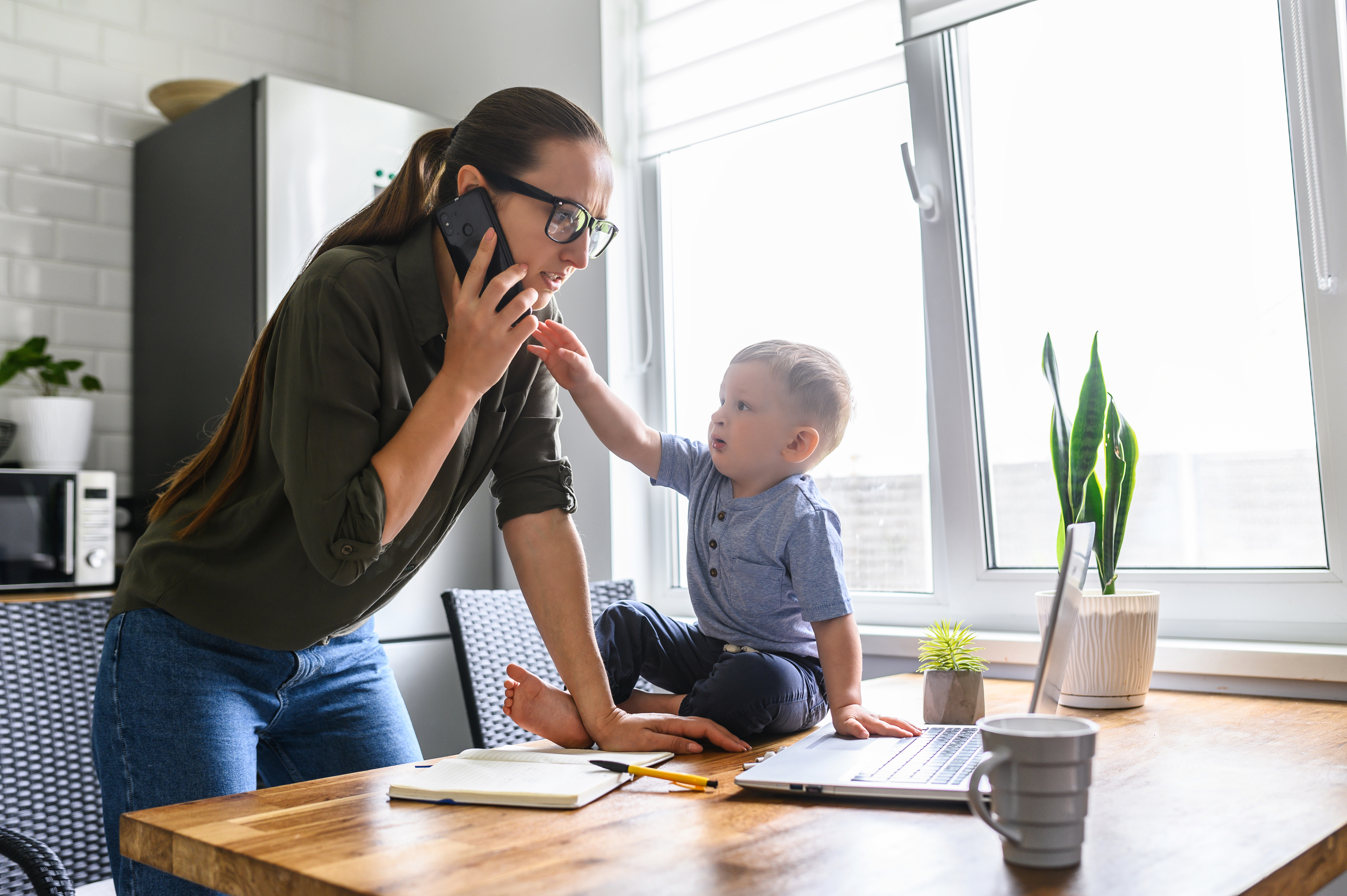Joven madre hablando por teléfono mientras su hijo pequeño lo agarra | Fuente: Shutterstock