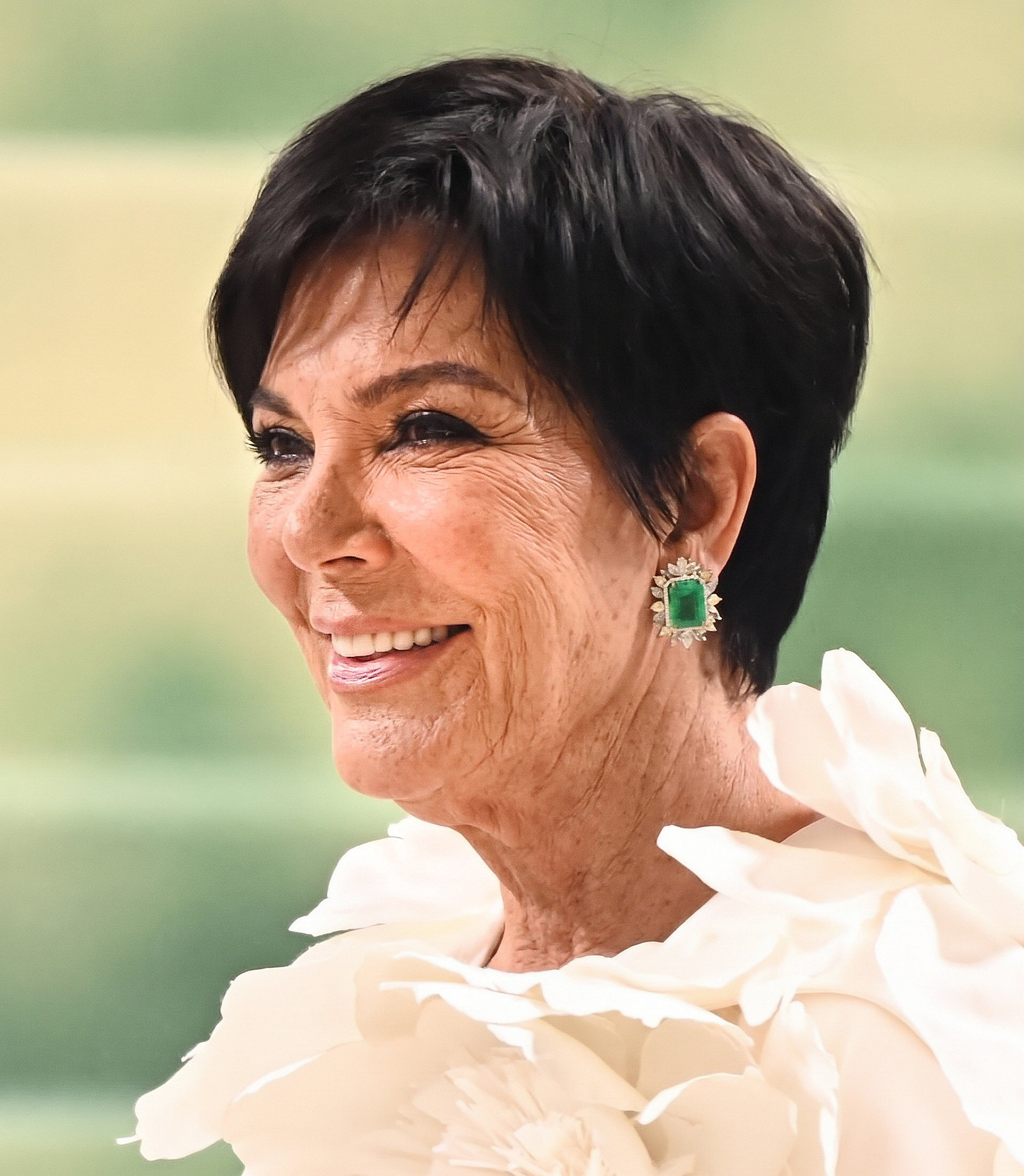 Kris, sonriente y con un elaborado conjunto blanco y unos pendientes verde esmeralda, cierra la primera sesión de IA, y sus arrugas naturales le dan un toque especial a este glamuroso retrato. | Fuente: Gemini