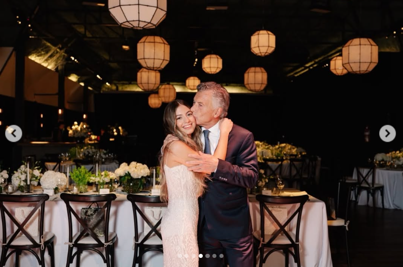 Mauricio Macri abraza tiernamente a su hija Antonia y le da un beso en la mejilla en el salón del evento, decorado con elegantes mesas y lámparas de seda colgantes. | Fuente: Instagram/mauriciomacri
