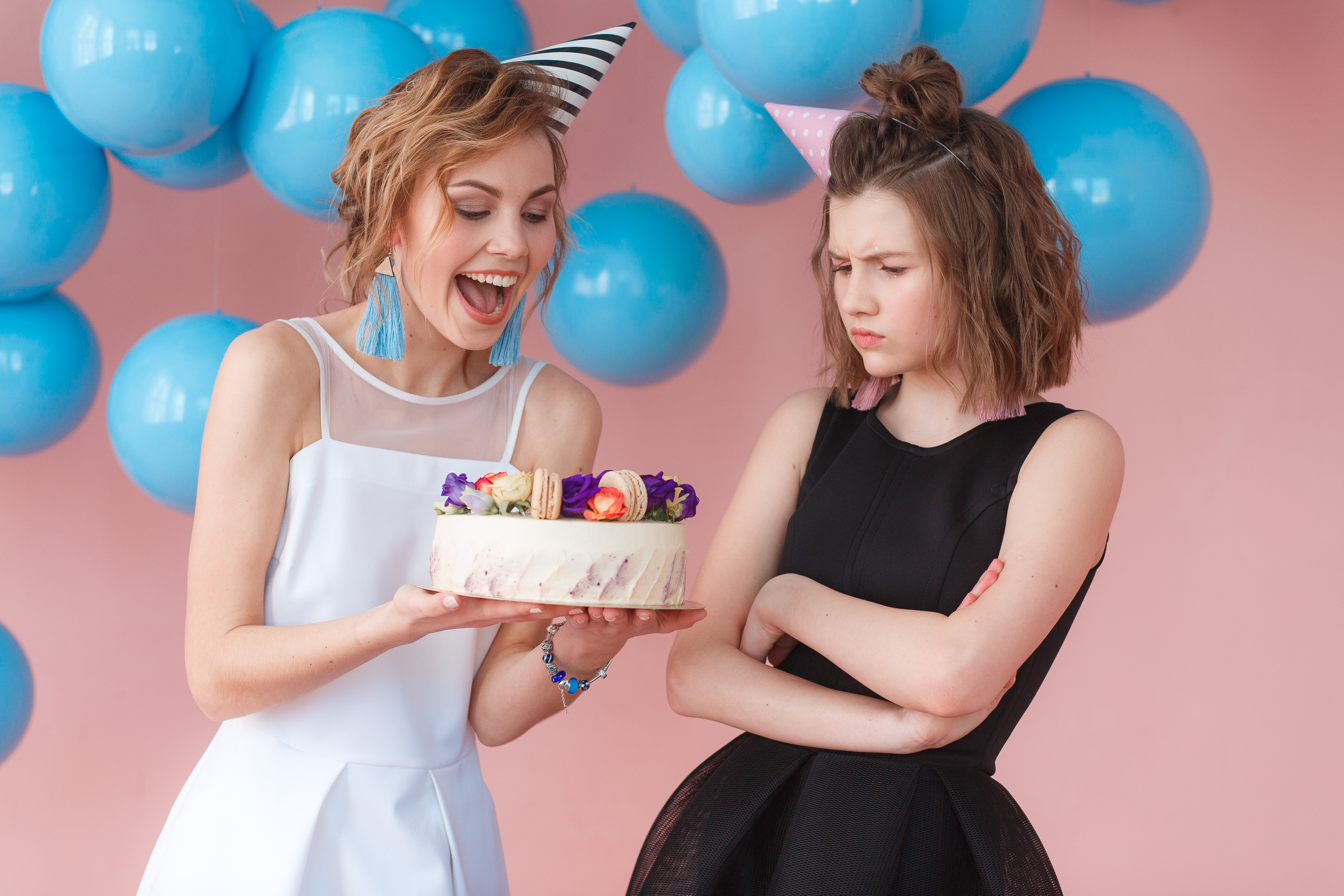 Dos adolescentes sosteniendo un pastel de cumpleaños, una sonriendo y la otra frunciendo el ceño | Fuente: Freepik