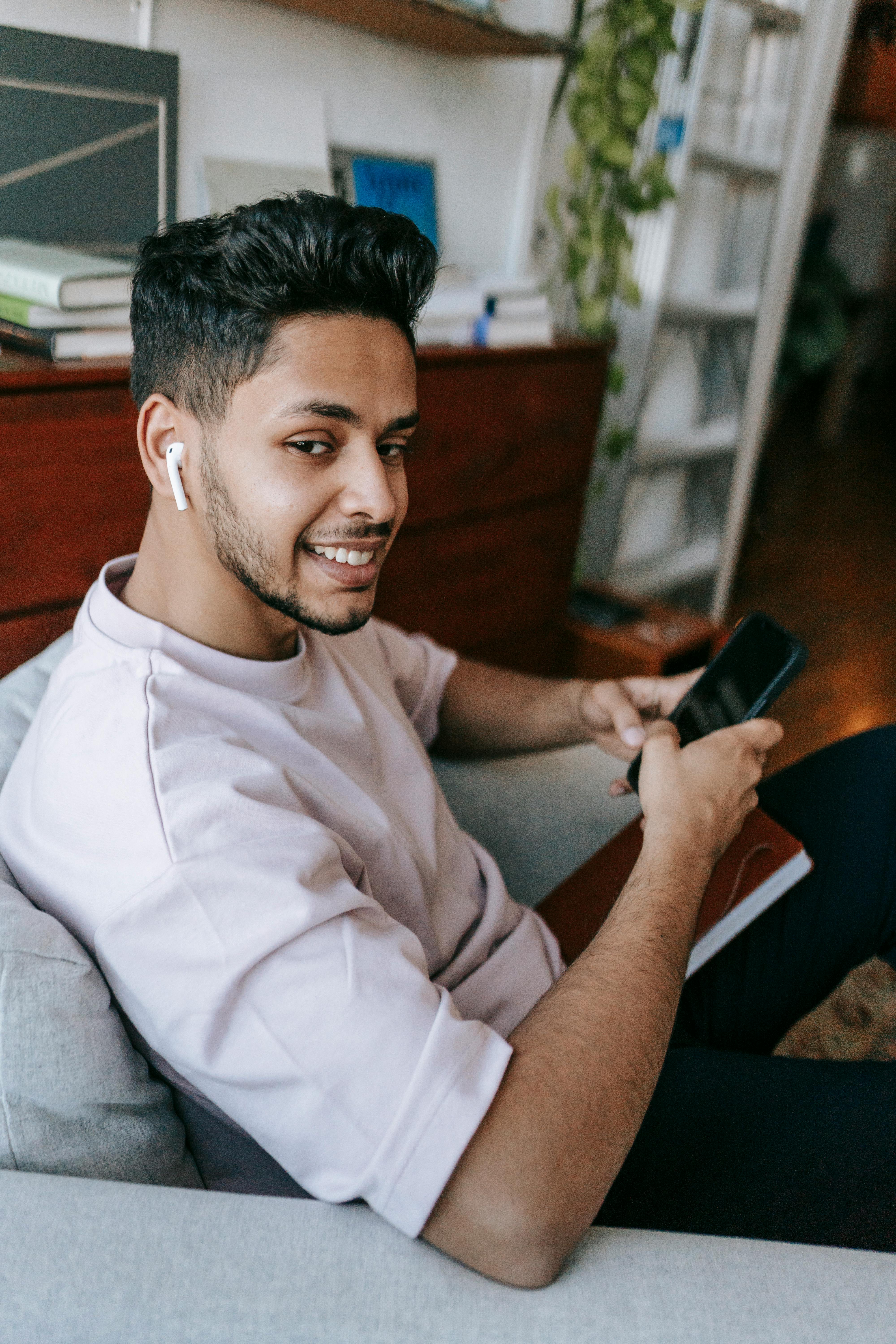 Un hombre feliz usando su teléfono y sus auriculares | Fuente: Pexels