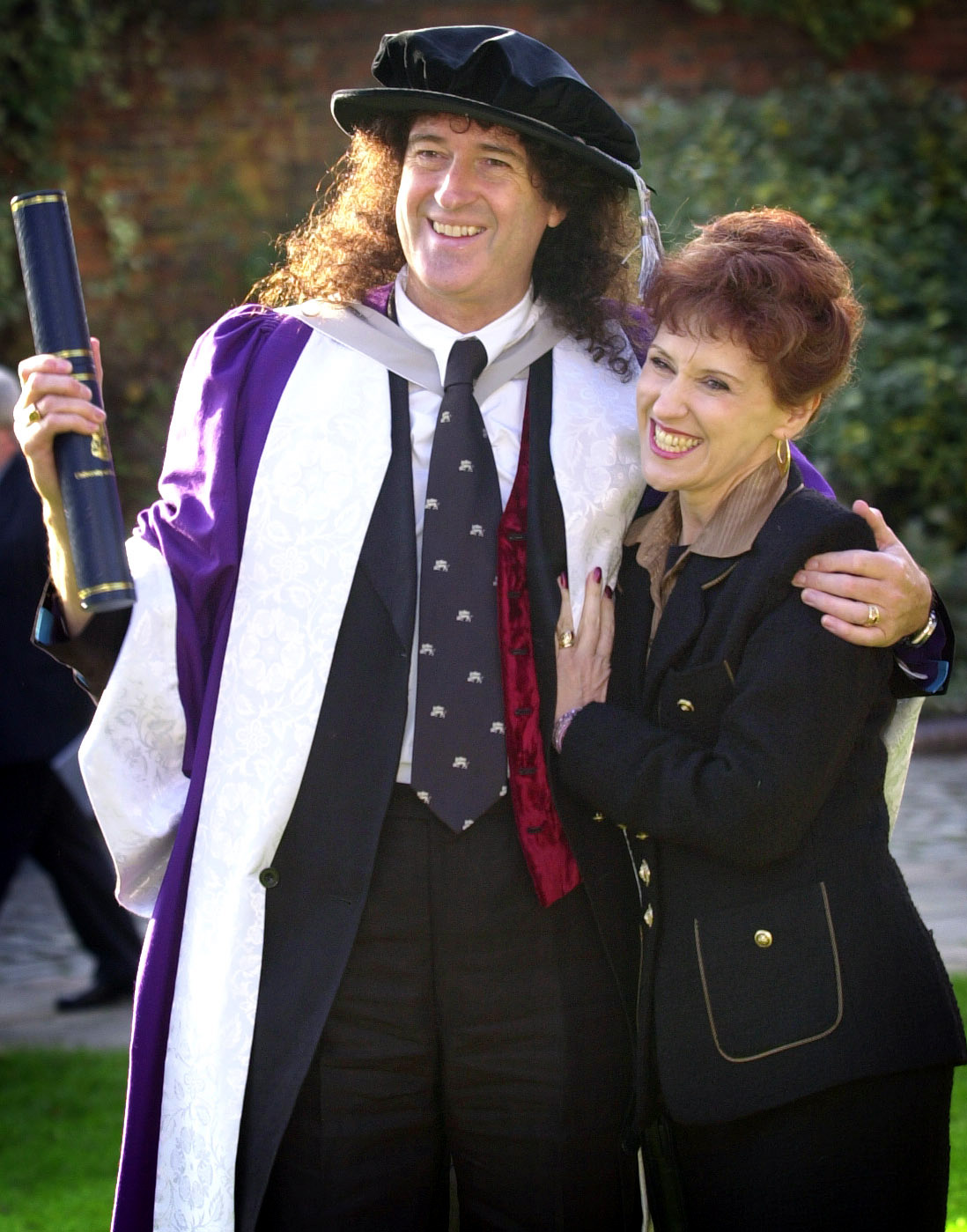 Brian May y Anita Dobson tras ser investido Doctor Honoris Causa en Ciencias por la Universidad de Hertfordshire, ante la catedral de St Albans, el 19 de noviembre de 2002 | Fuente: Getty Images