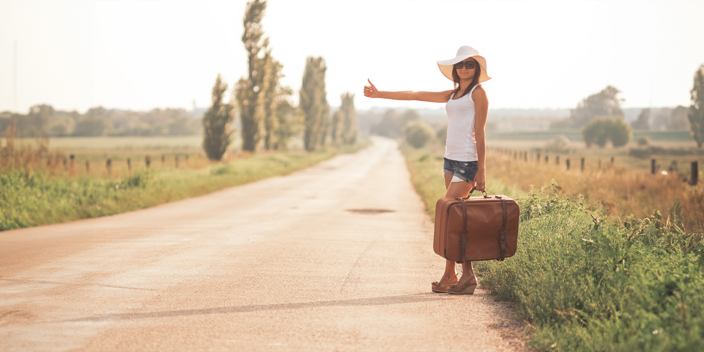 Mujer joven con una maleta en una carretera | Fuente: Shutterstock