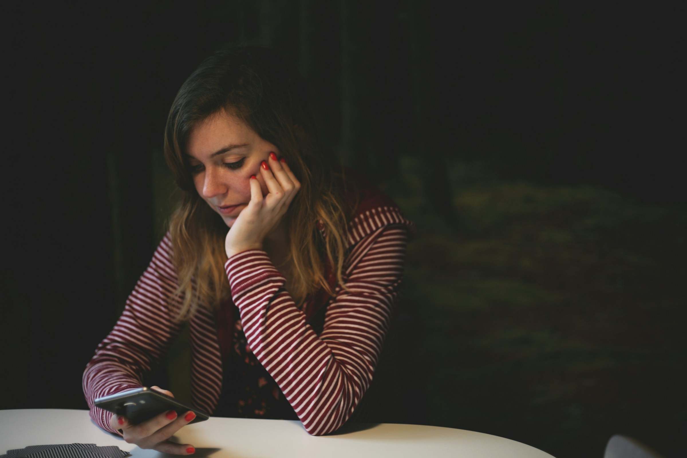 Mujer joven mirando pensativa su teléfono | Fuente: Unsplash