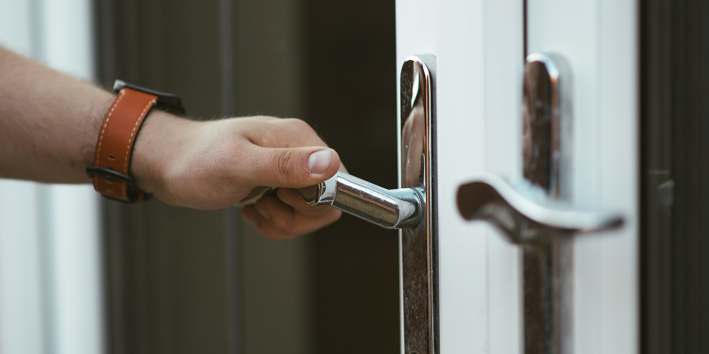 La mano de un hombre agarrando la manilla plateada de una puerta | Fuente: Shutterstock