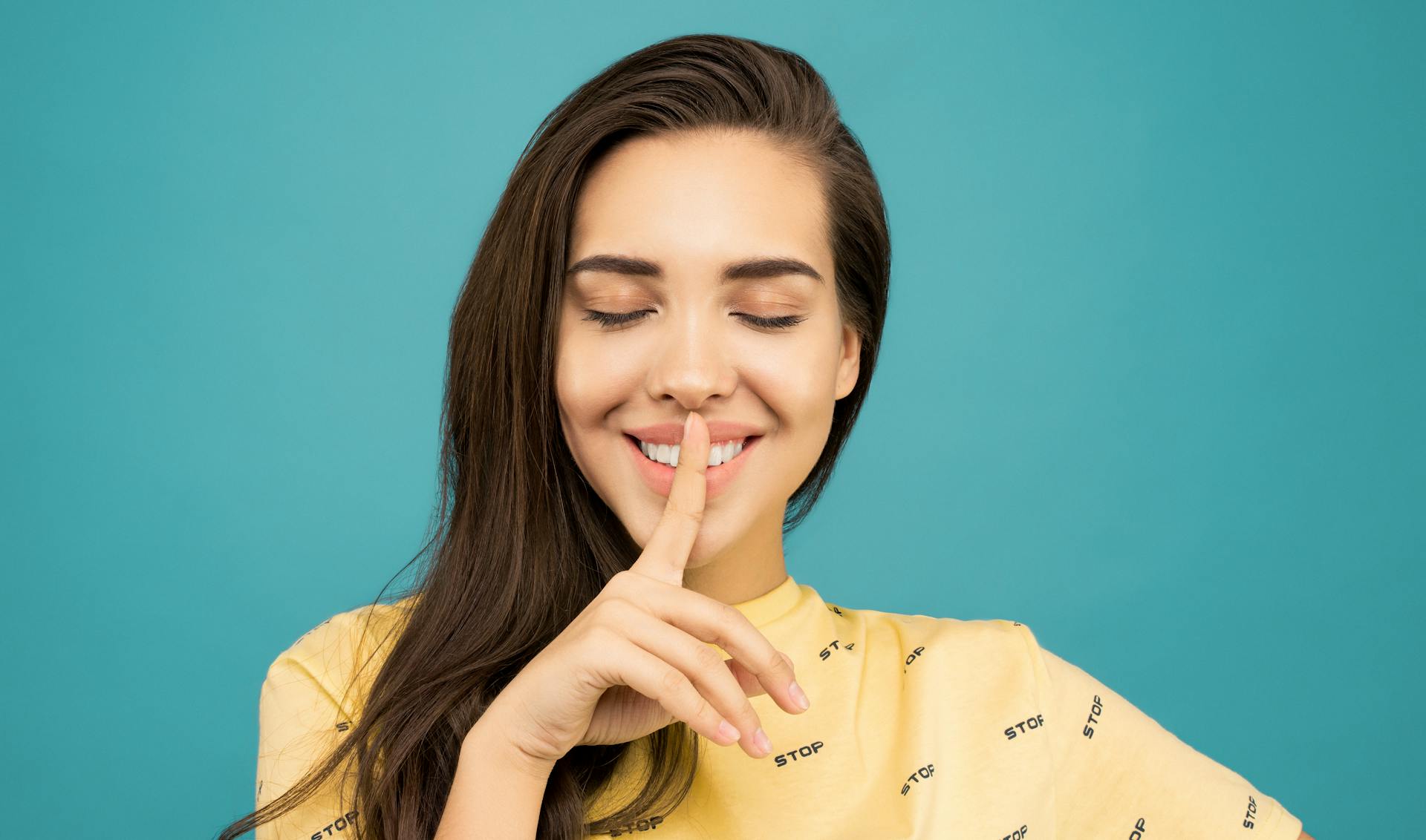 Una mujer sonriente con un dedo apretado contra los labios | Fuente: Pexels
