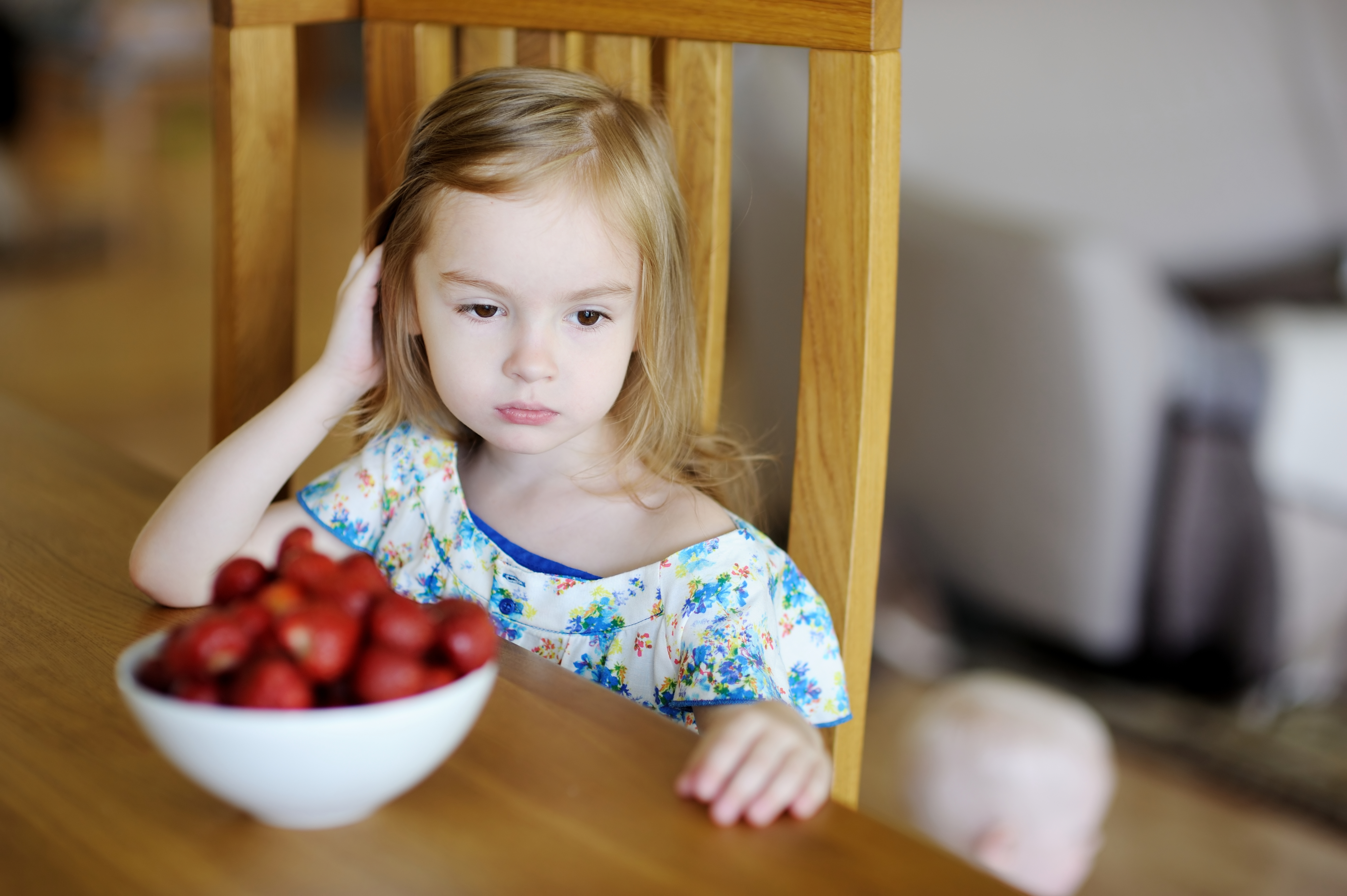 Niña con mirada triste con un cuenco de fresas delante de ella en la mesa del comedor | Foto: Shutterstock