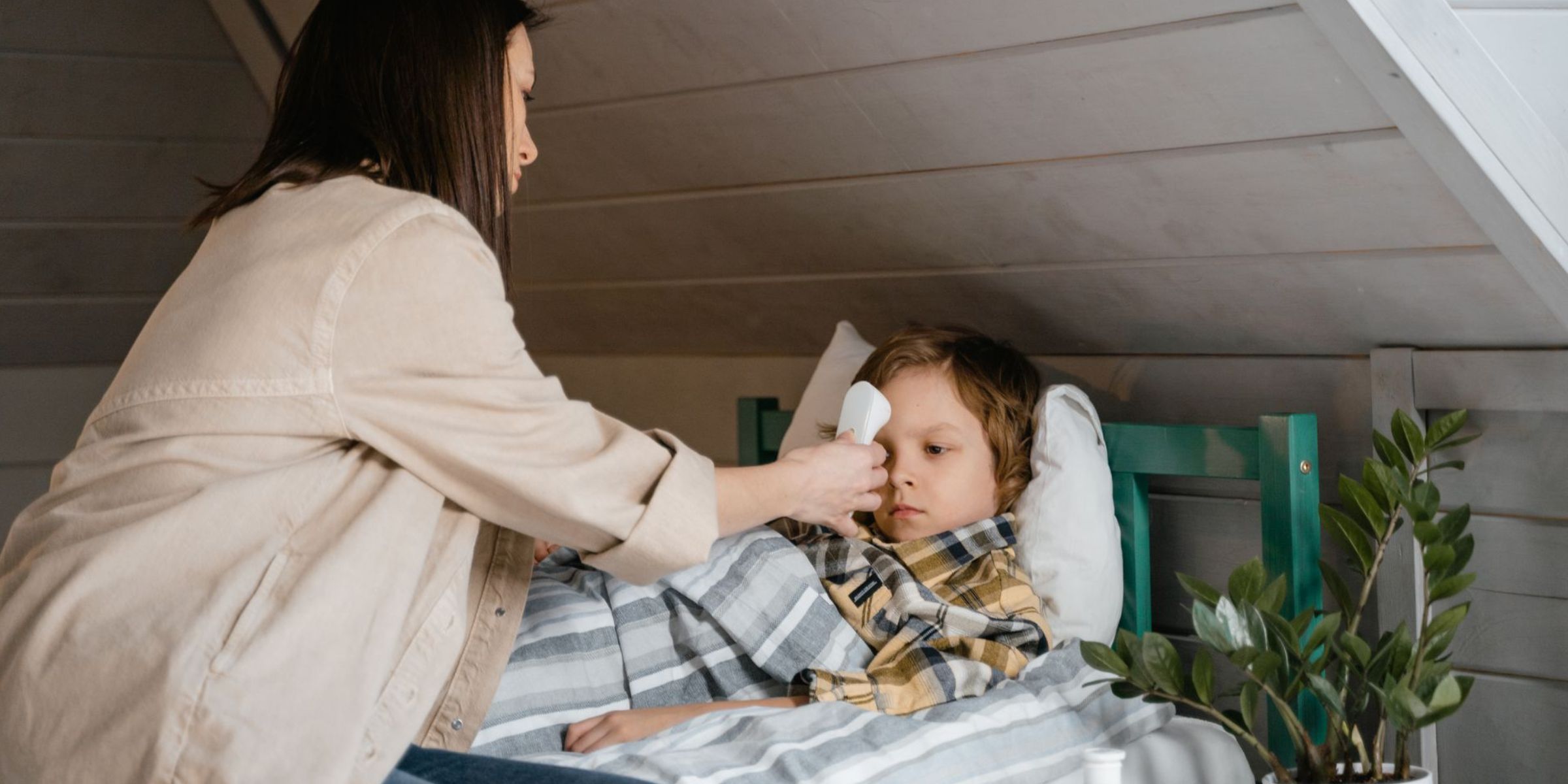 Una madre le toma la temperatura a su hijo enfermo mientras descansa en la cama | Fuente: Pexels
