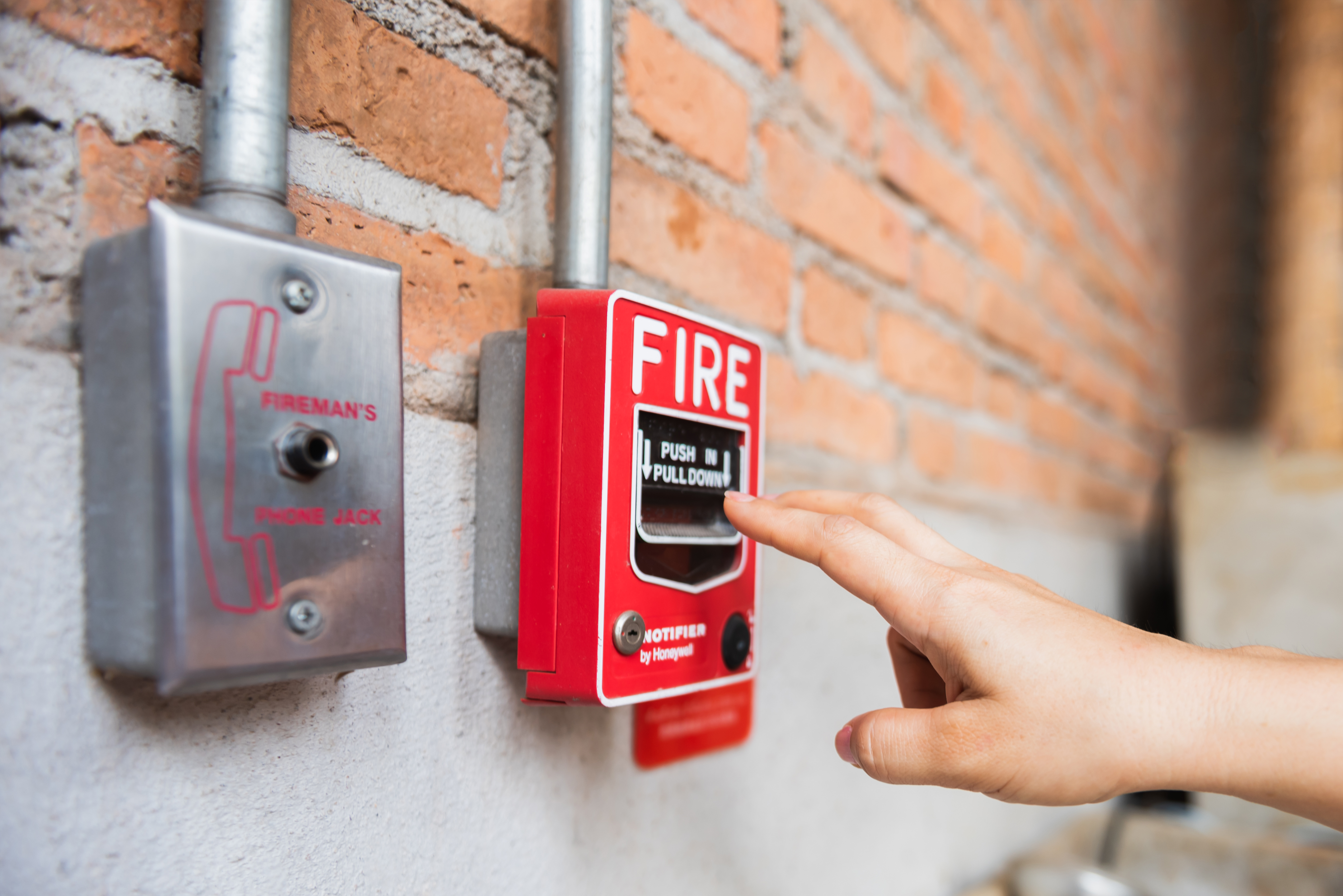 Mano de mujer alcanzando el interruptor del sistema de alarma de incendios | Foto: Getty Images