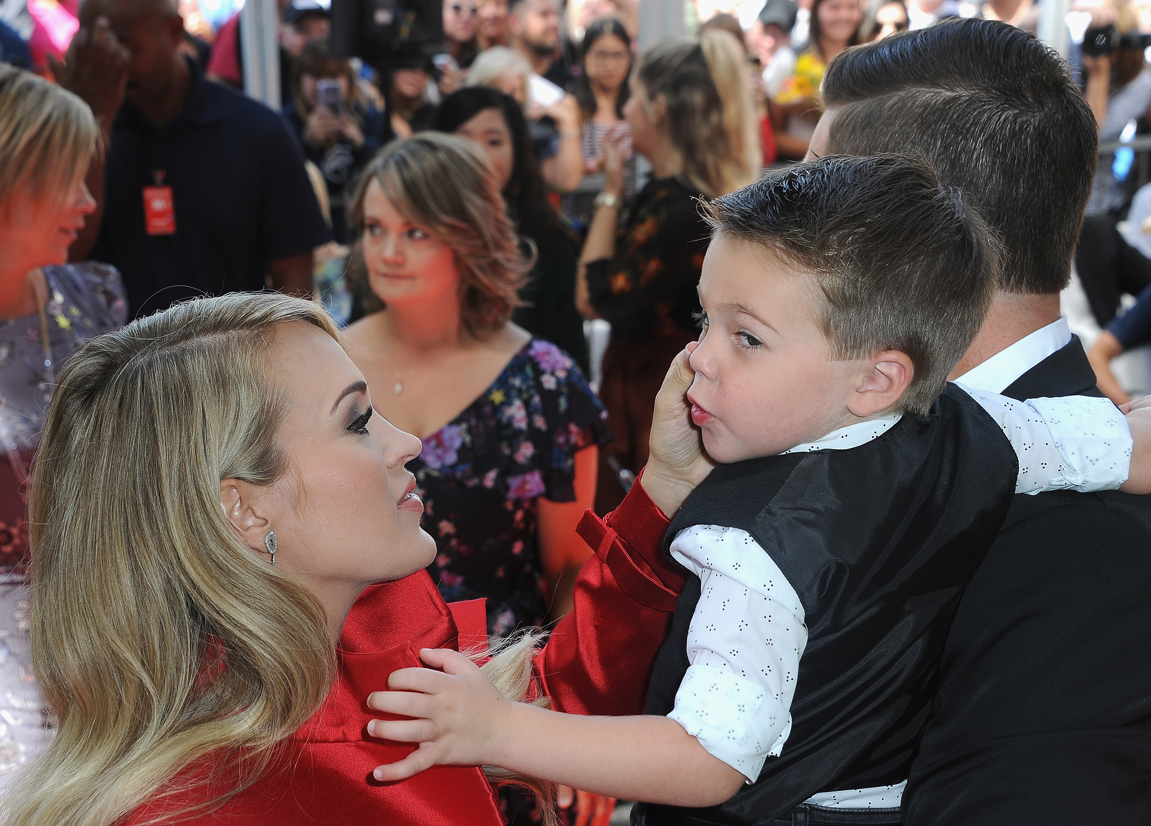 Carrie Underwood comparte un momento tierno con su hijo mayor, Isaiah, mientras su esposo, Mike Fisher, lo sostiene en brazos en un evento de 2018. Carrie y Mike dieron la bienvenida a su segundo hijo, Jacob, en enero de 2019. | Fuente: Getty Images.