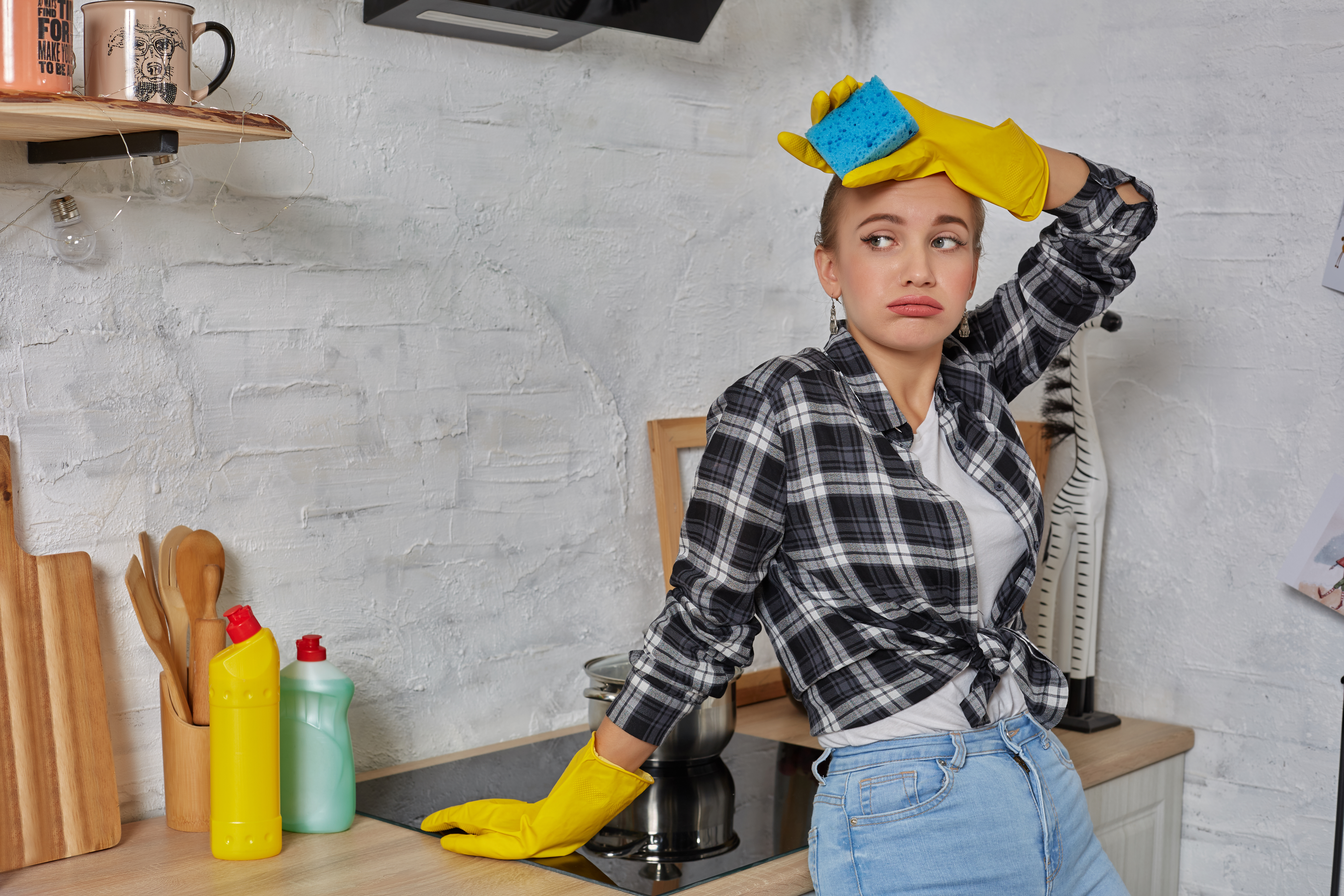 Mujer con cara de harta mientras está sentada junto a la encimera de la cocina fregando | Fuente: YuliiaKa en Freepik