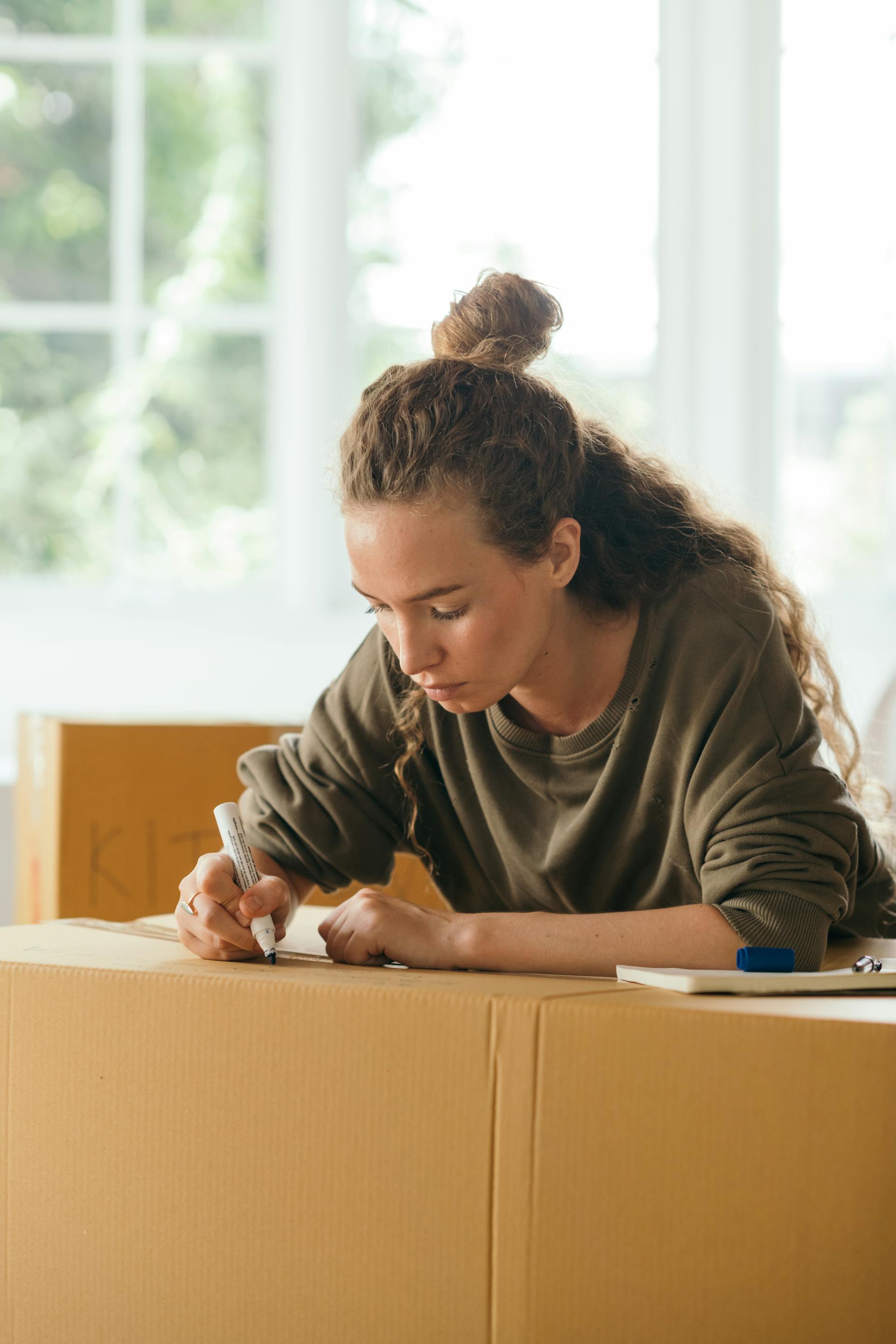 Una mujer escribiendo en una caja en movimiento | Fuente: Pexels