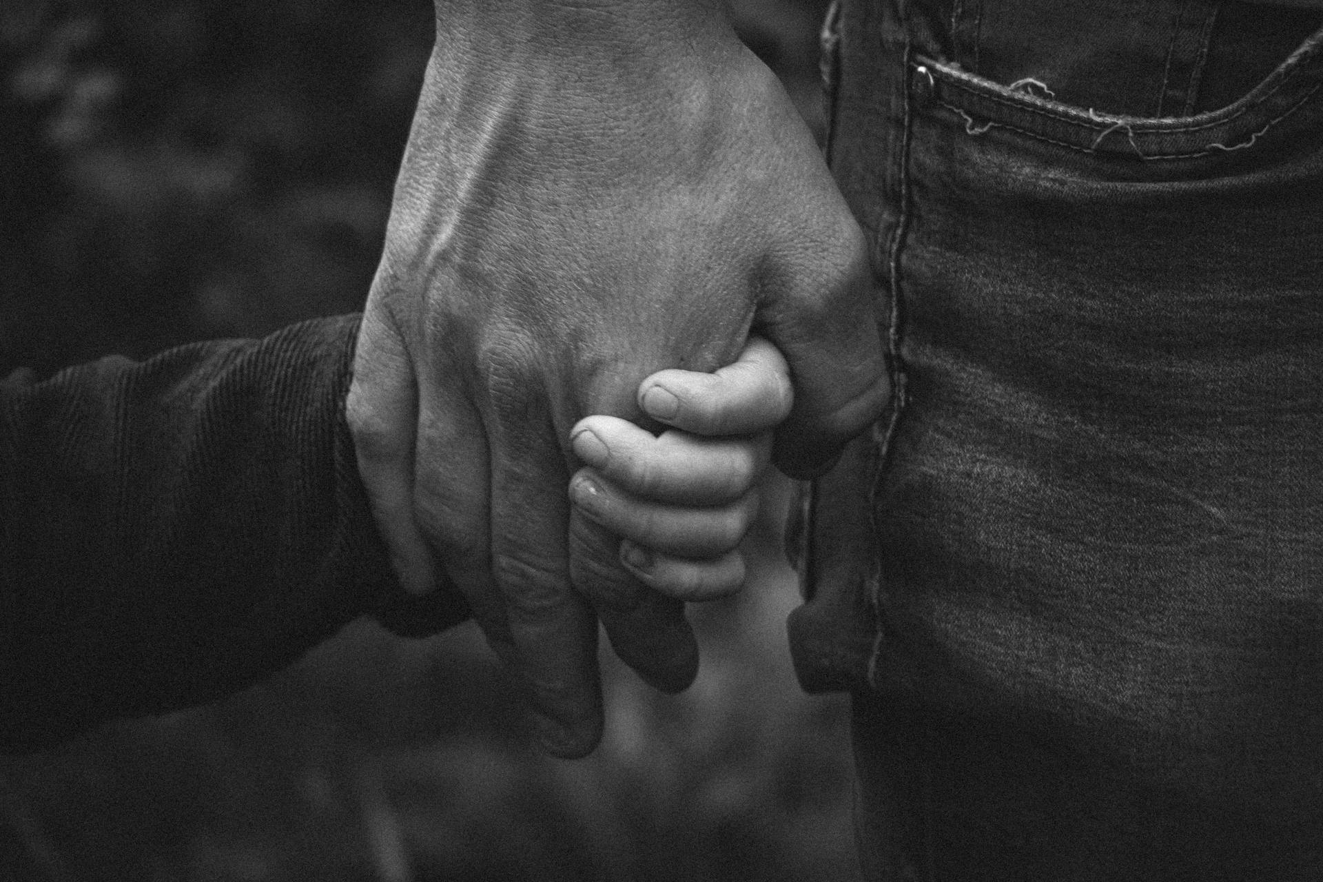 Toma en escala de grises de un hombre tomando la mano de una niña | Fuente: Pexels