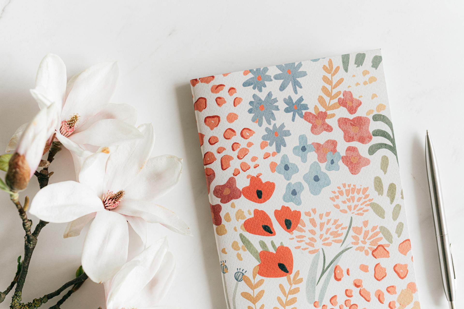 Un'agenda e una penna vicino a dei fiori bianchi | Fonte: Pexels