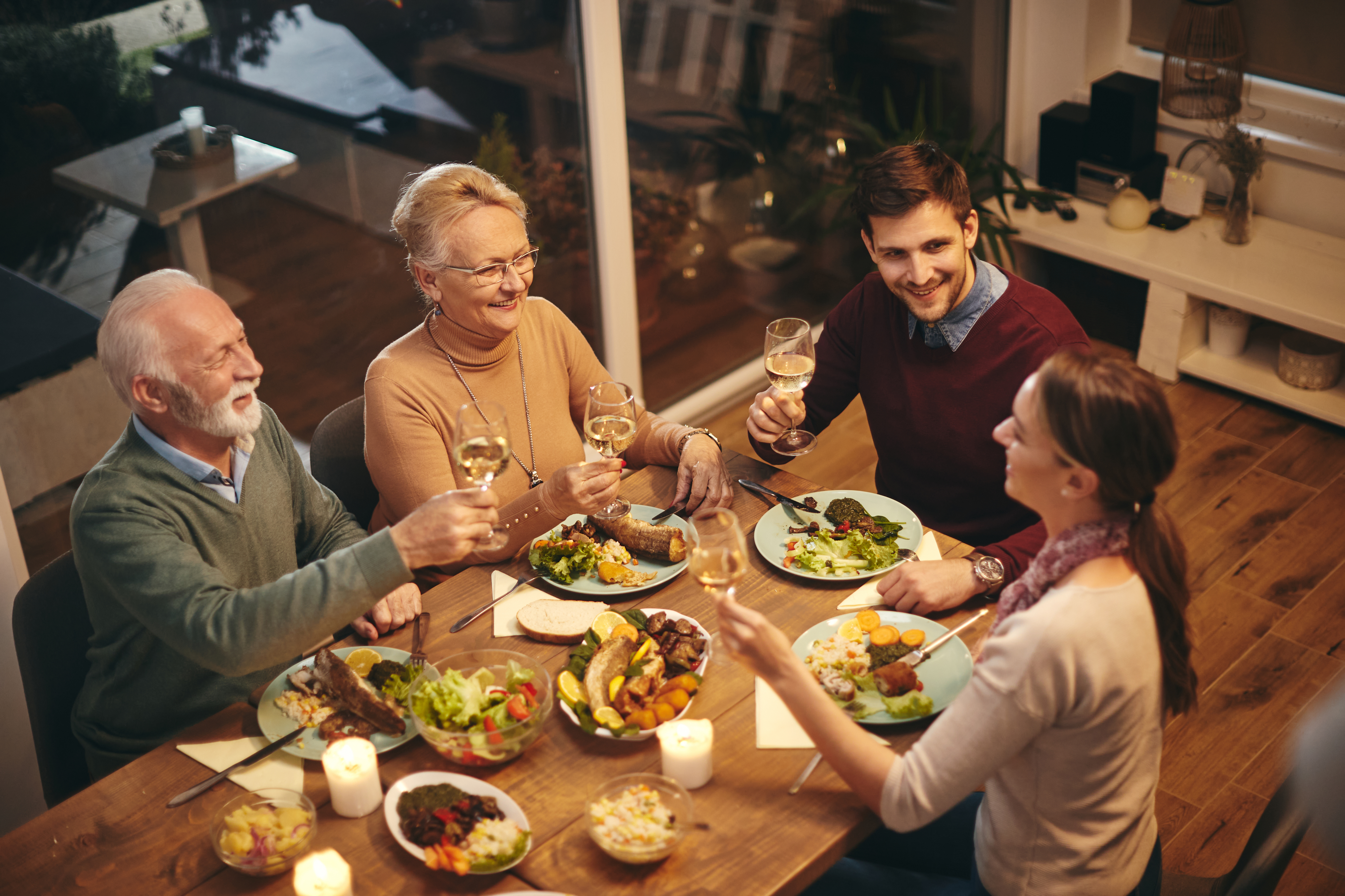 Una mujer mayor feliz brinda con su familia mientras come en la mesa del comedor | Fuente: Shutterstock