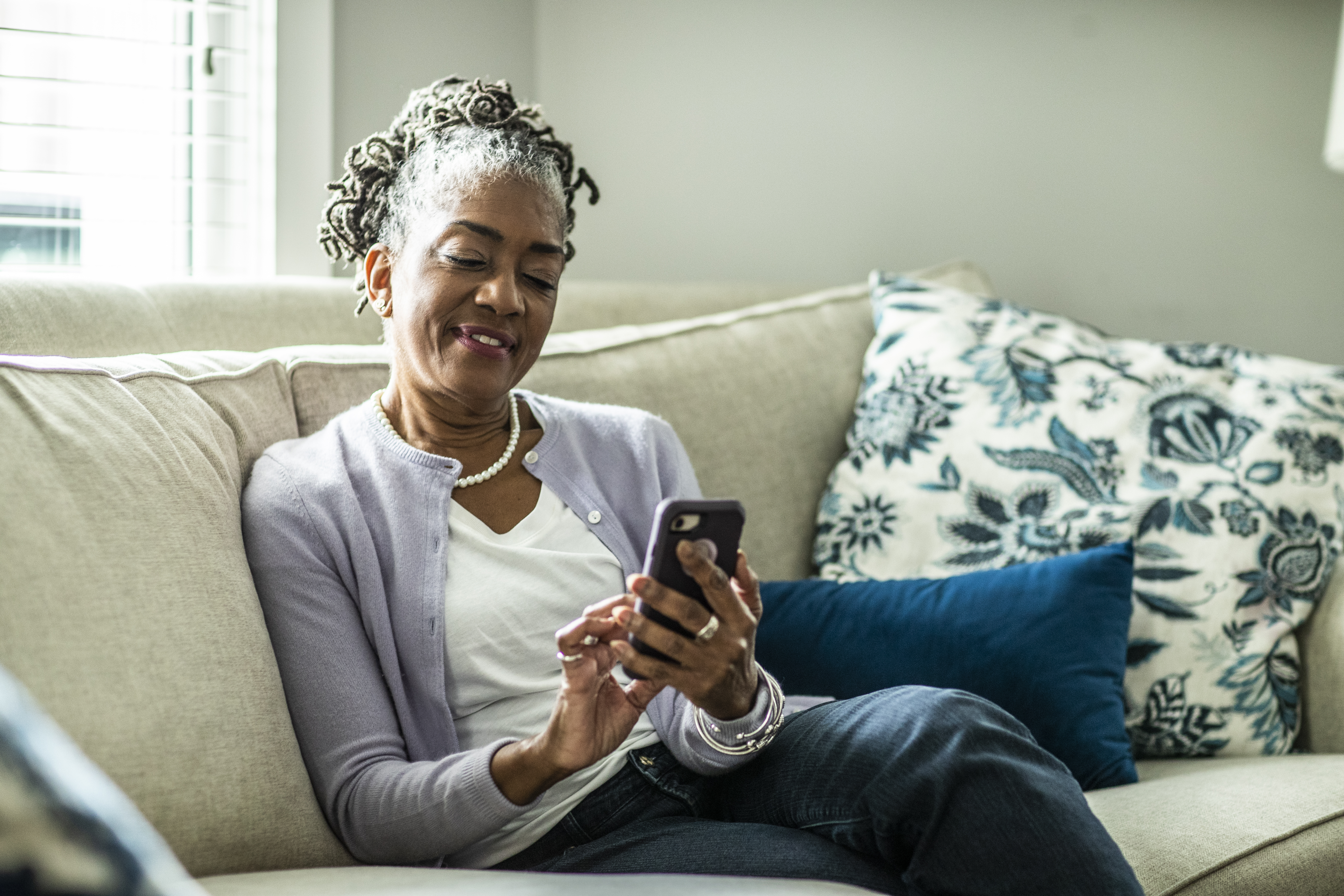 Mujer mayor utilizando un smartphone en el salón de una casa de las afueras | Foto: Getty Images