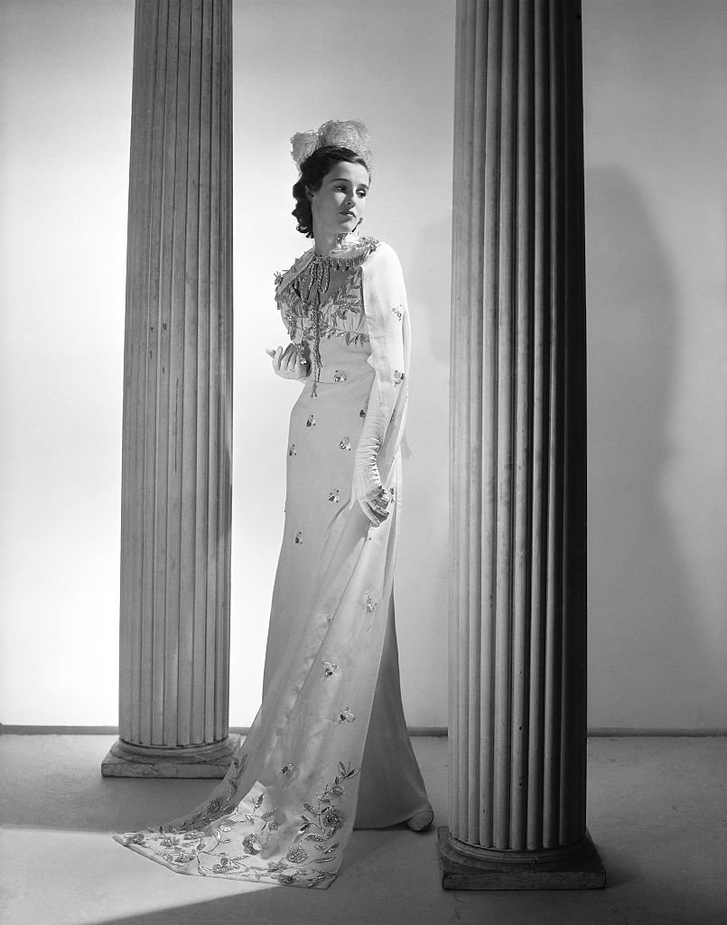 Barbara Cushing de pie entre dos columnas, con un vestido bordado y un tocado de plumas. | Foto: Getty Images