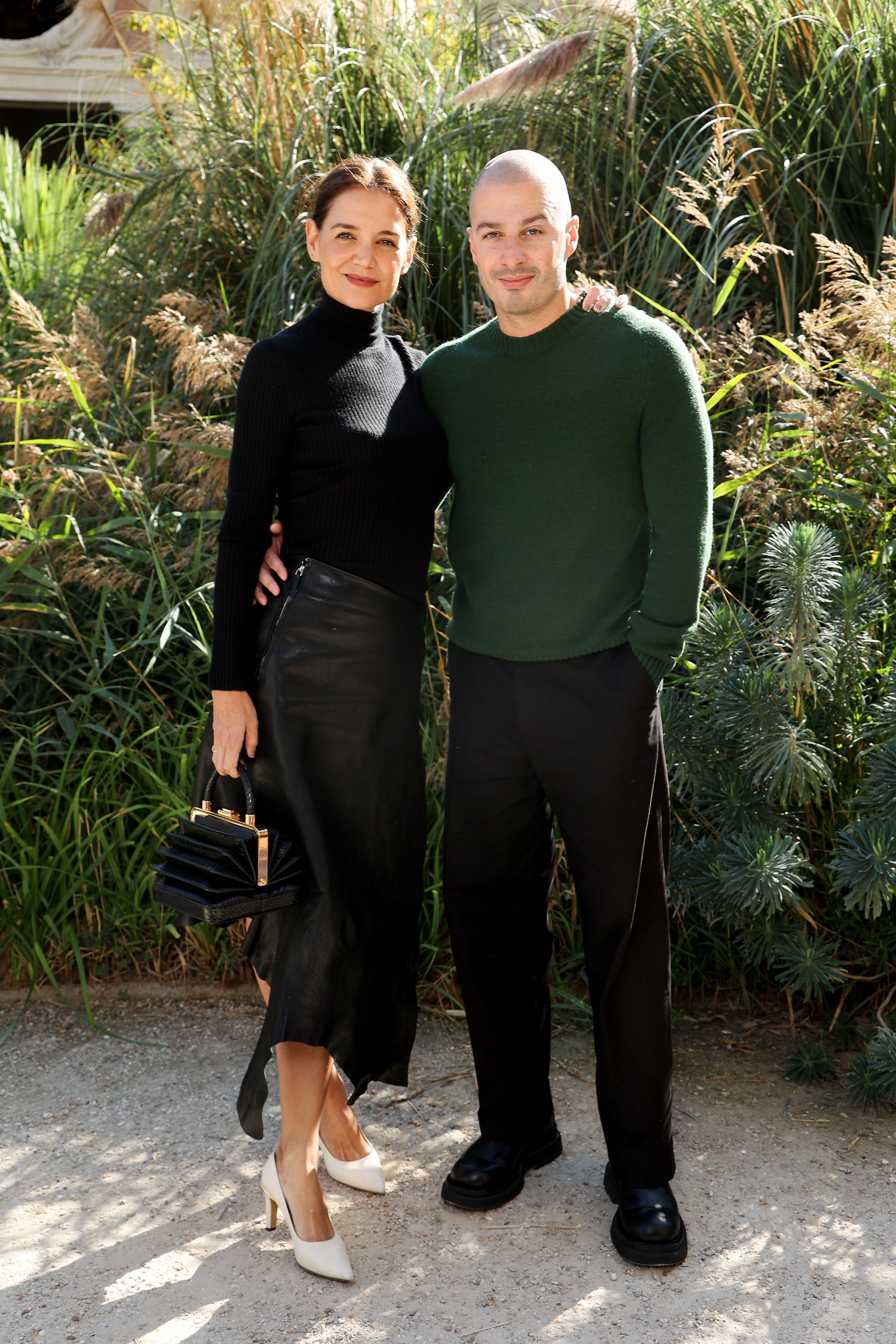 Unos zapatos de salón blancos de punta rompen la monotonía del conjunto, por lo demás negro, de Katie Holmes, mientras que el jersey verde bosque de Jason Bard Yarmosky aporta el toque de color más llamativo a su lado. La actriz y el artista llegaron juntos al desfile de primavera/verano 2027 de Gabriela Hearst en París. | Fuente: Getty Images