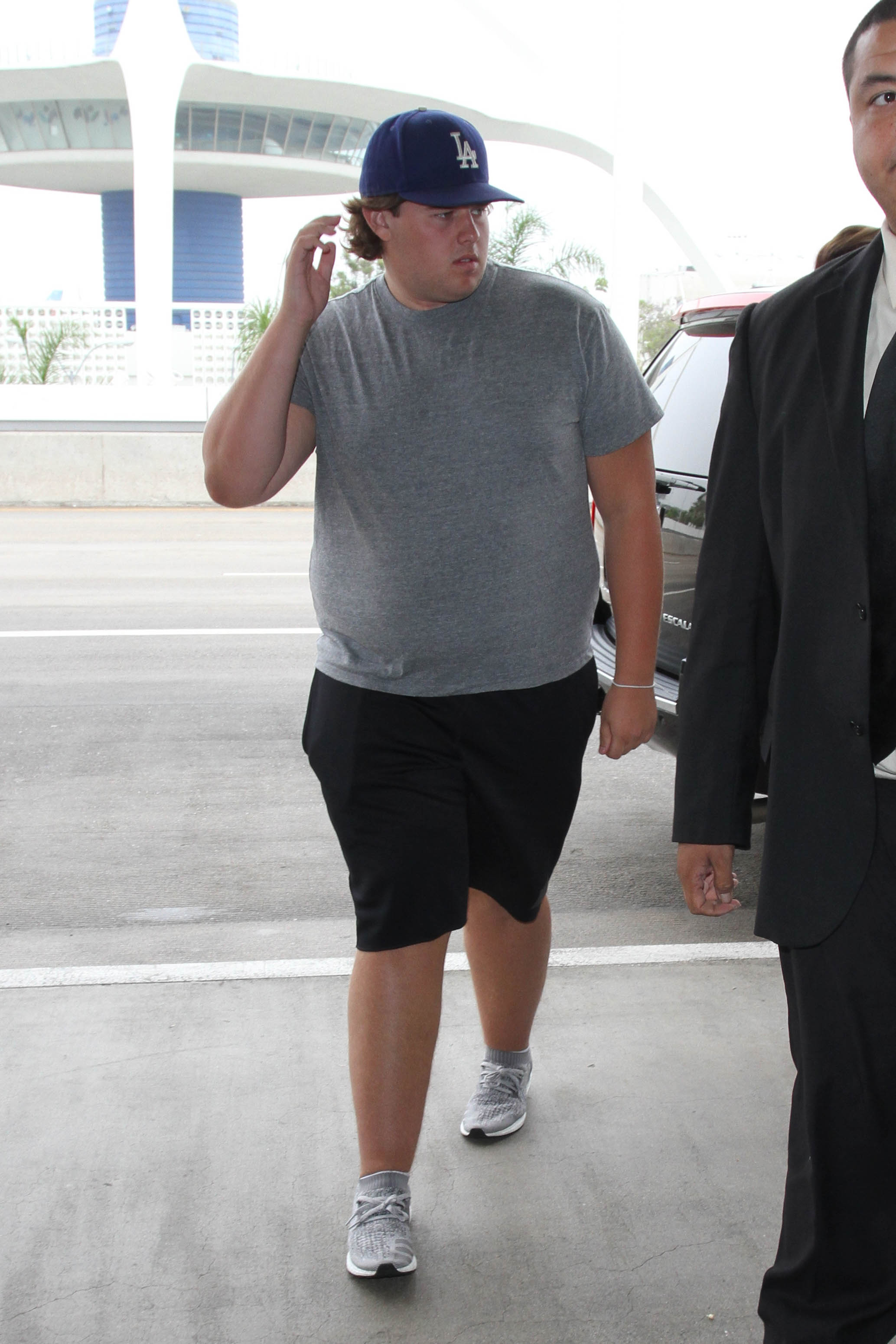Christopher Schwarzenegger aparece en el aeropuerto de Los Ángeles el 31 de agosto de 2016 con camiseta gris, gorra azul de los LA Dodgers, mochila verde y equipo militar, luciendo una complexión más robusta y concentrado en sus pertenencias.