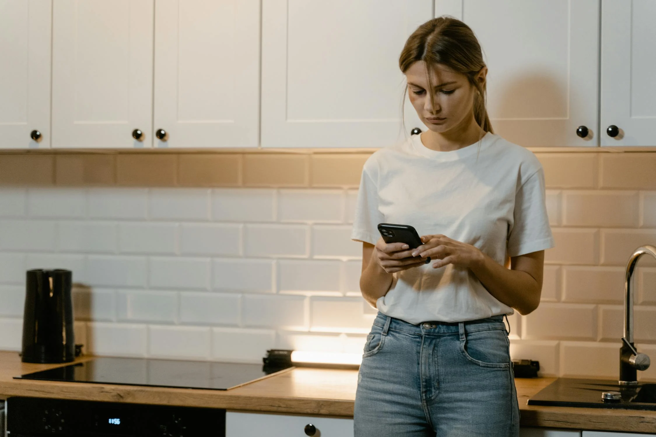 Una mujer tecleando en su teléfono en la cocina de su casa | Fuente: Pexels