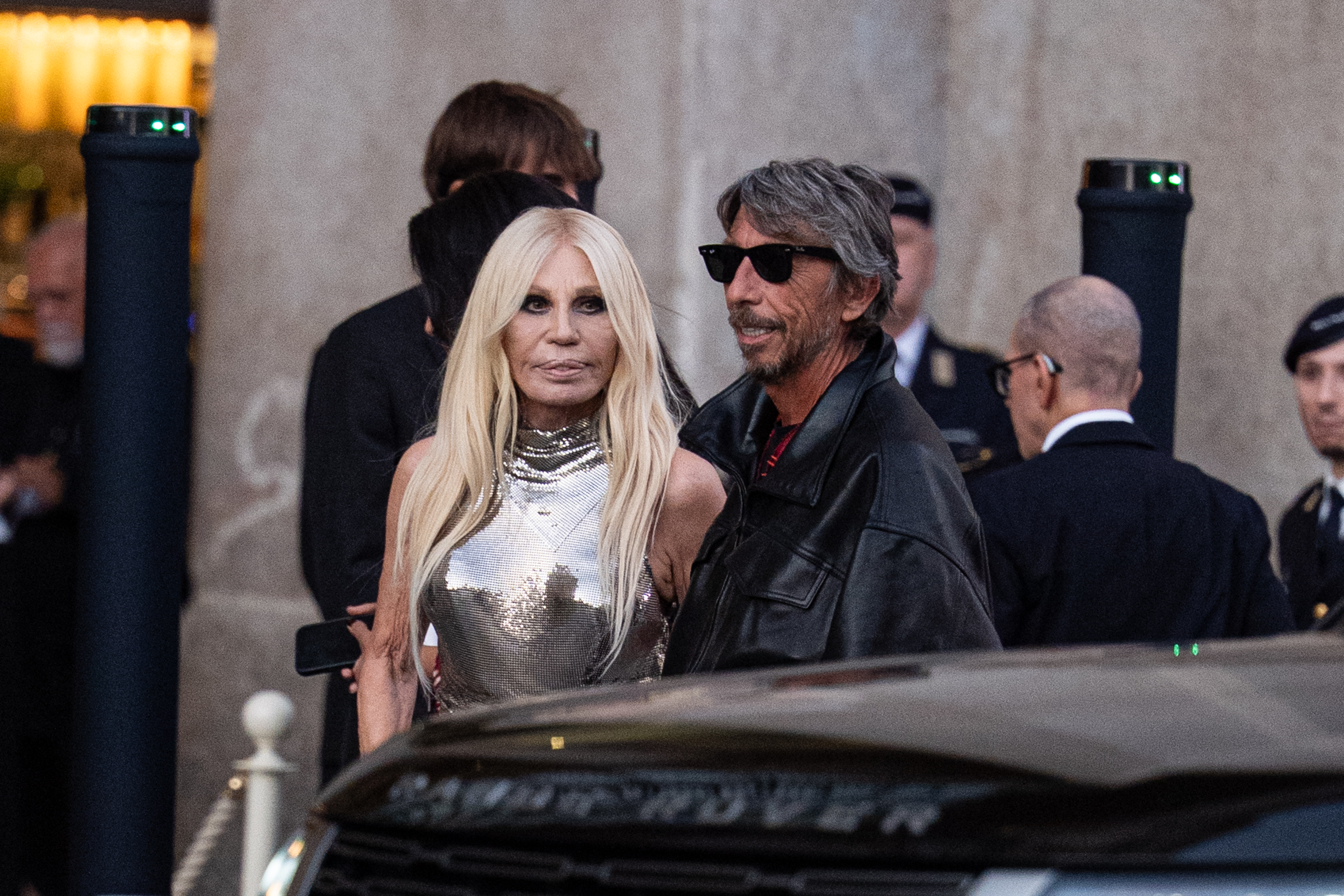 Versace aparece junto a Pierpaolo Piccioli, y en el primer plano se aprecia su top plateado brillante y su larga melena rubia platino. | Fuente: Getty Images