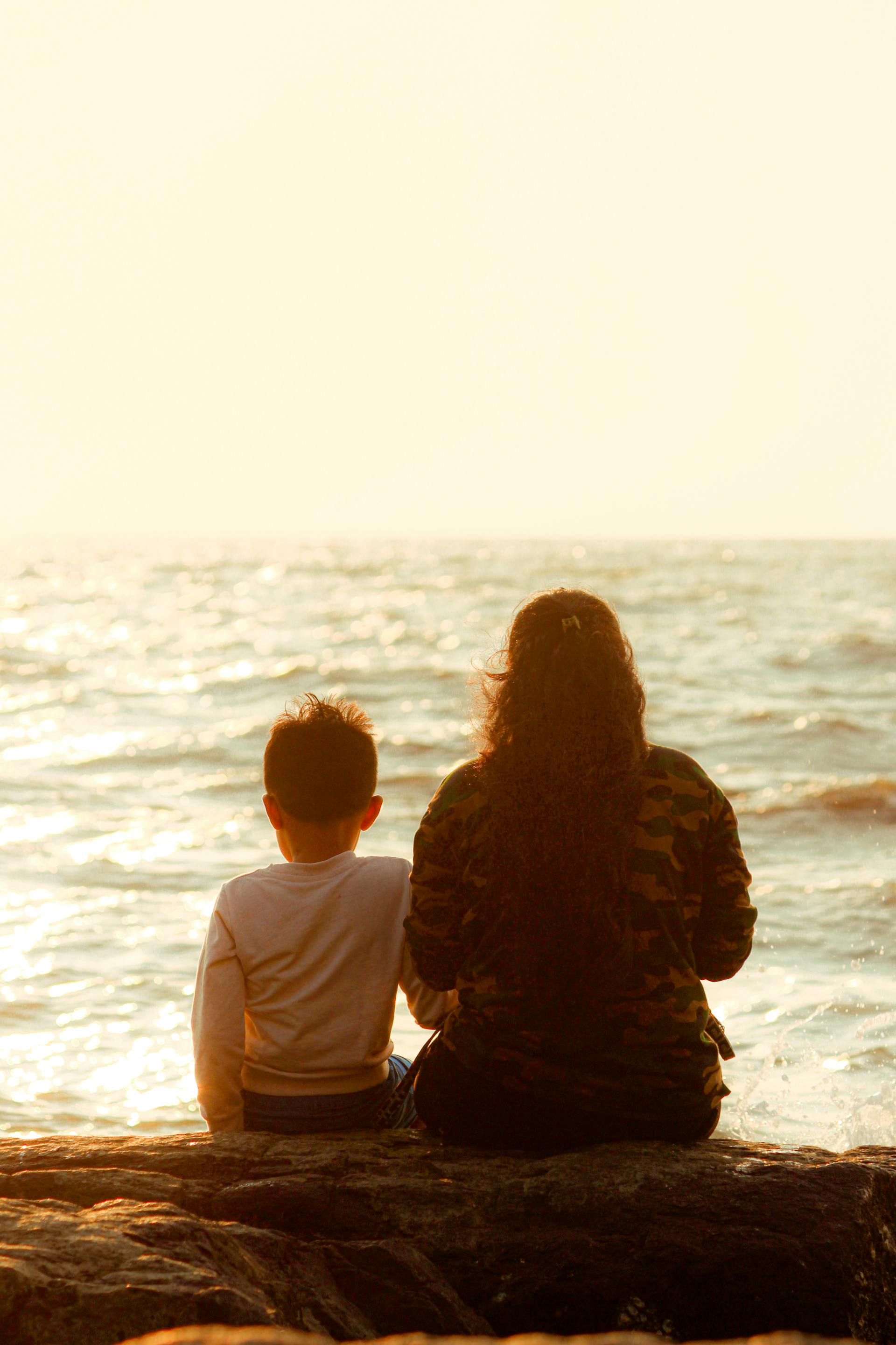 Una madre sentada con su hijo en la orilla del mar | Foto: Pexels