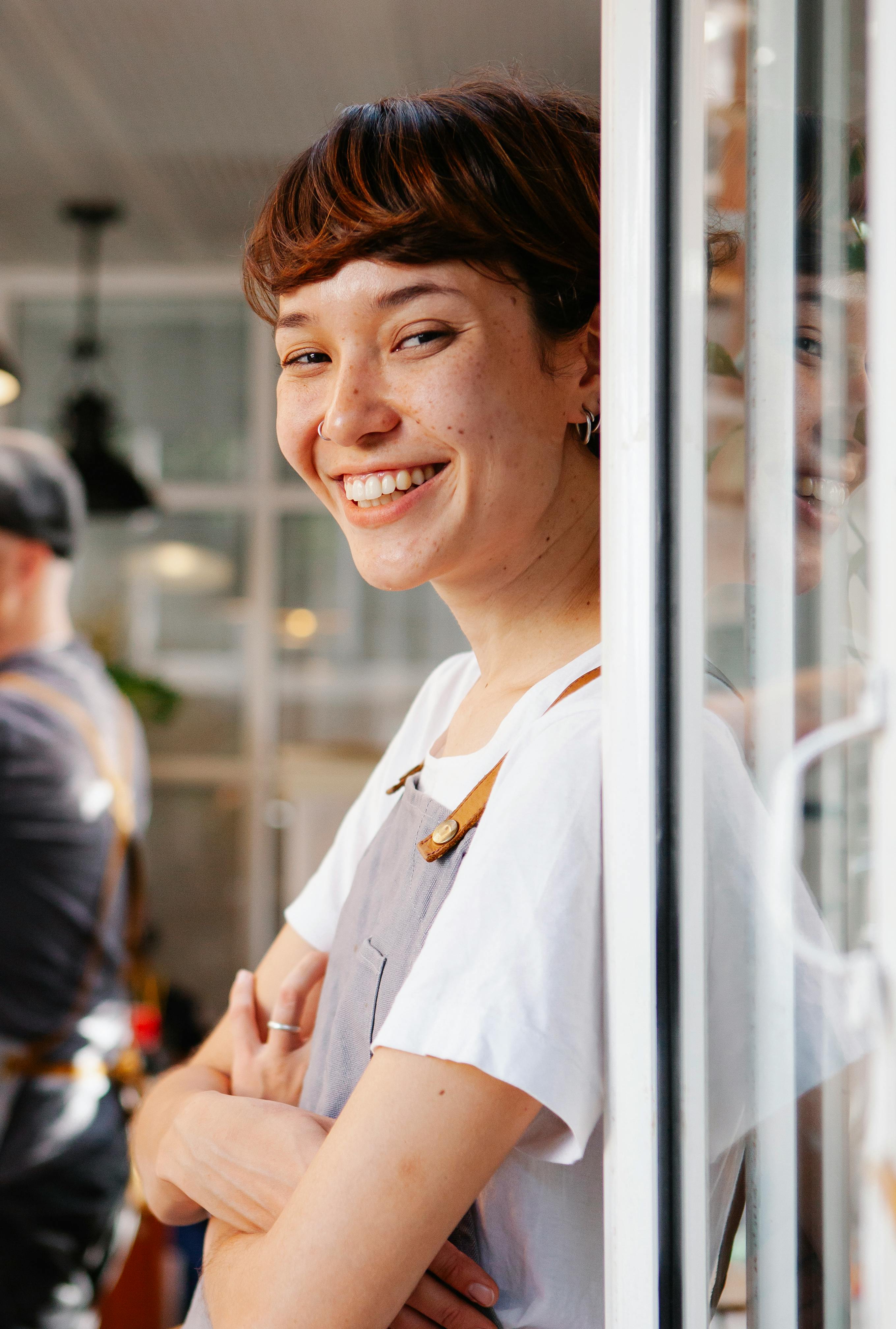 Una camarera feliz en la puerta de un restaurante | Fuente: Pexels