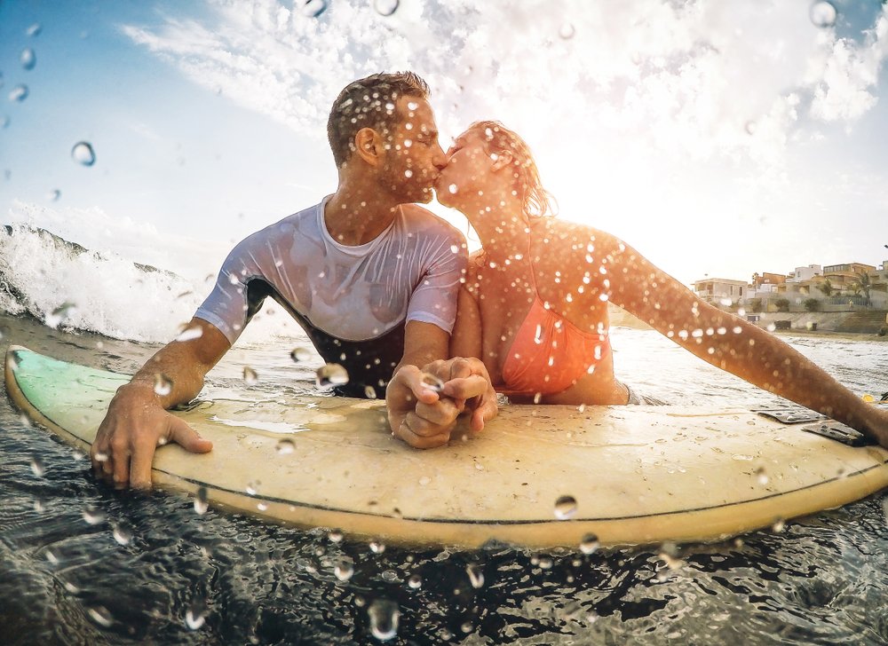 Feliz pareja deportiva besándose mientras surfea en el mar. | Foto: Shutterstock