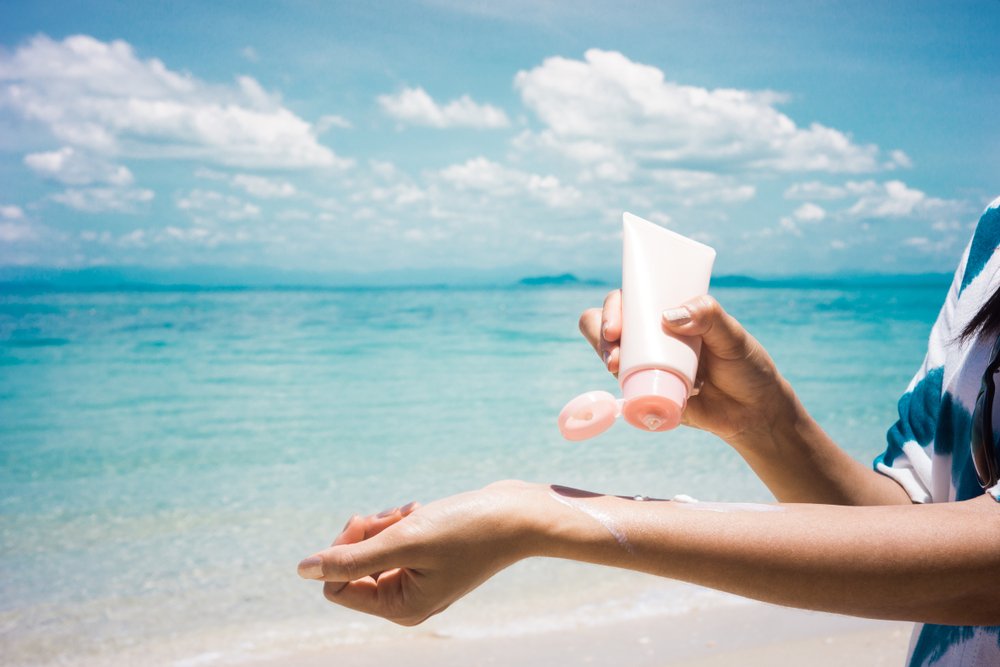 Mujer aplicando protector solar en sus manos en la playa. | Fuente: Shutterstock