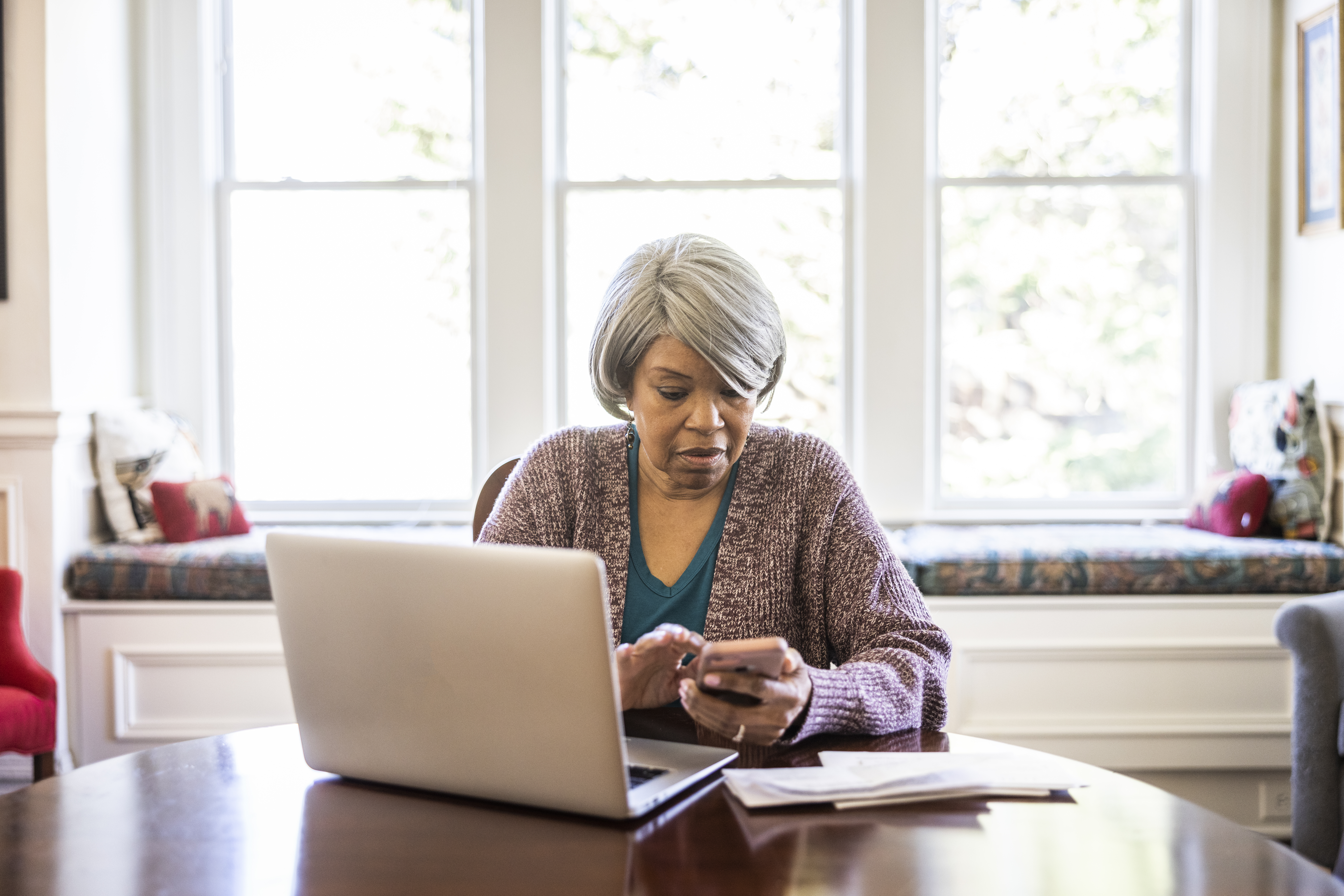Mujer mayor pagando facturas con un portátil y un smartphone en casa | Foto: Getty Images