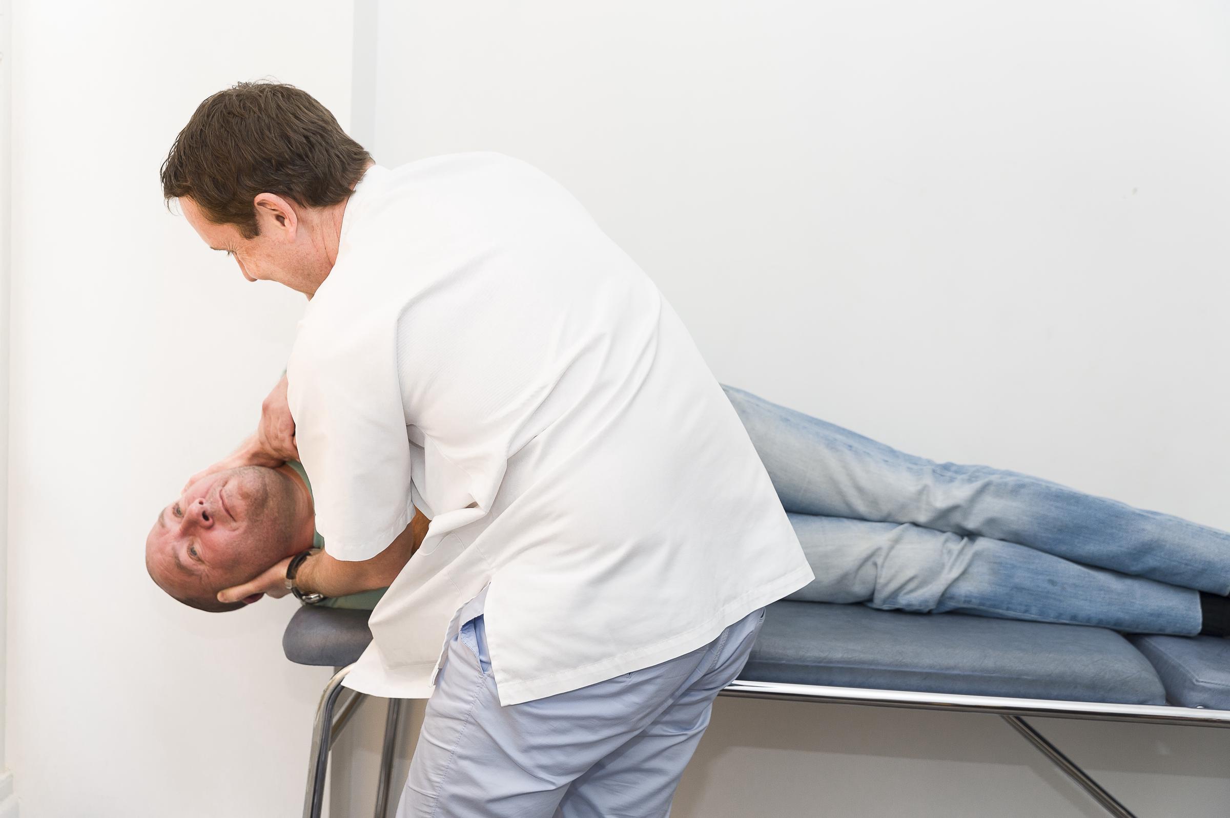 Un médico coloca a un paciente en posición para una maniobra diagnóstica utilizada habitualmente en las evaluaciones otorrinolaringológicas, posiblemente para evaluar el vértigo o el sistema vestibular | Fuente: Getty Images